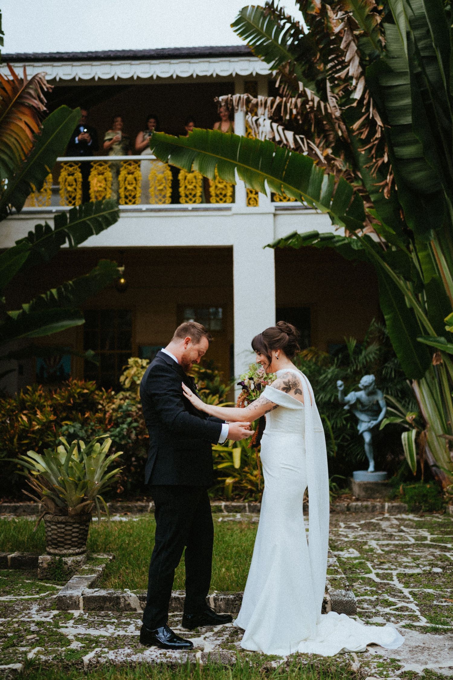 Bride and groom share an intimate first look moment in a tropical garden courtyard with lush greenery.