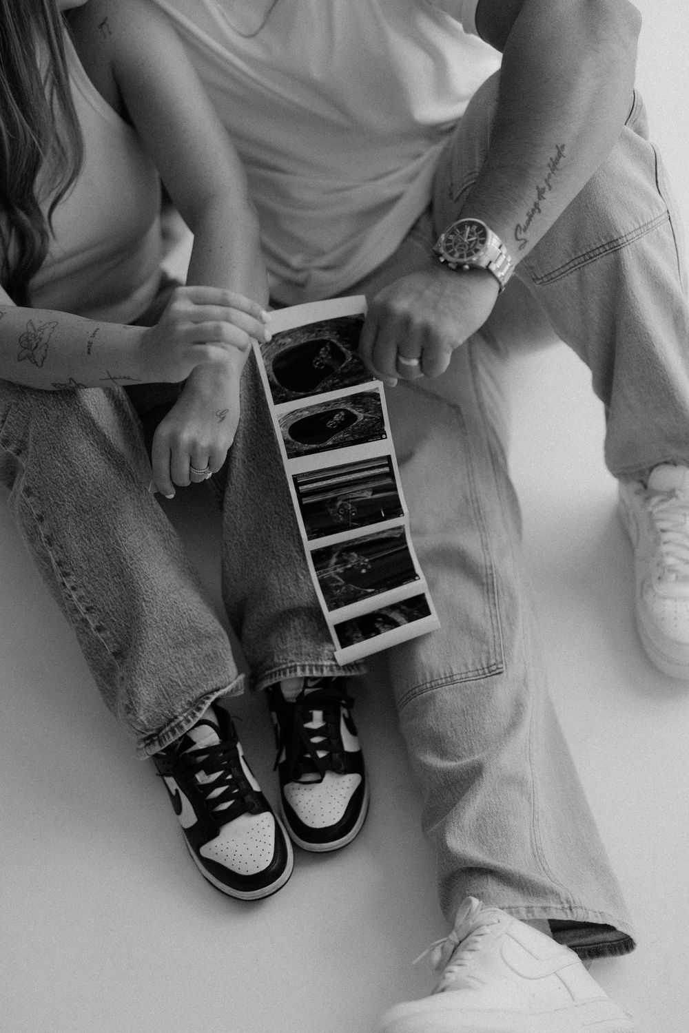 Black and white series showing ultrasound photos being held next to baby shoes on a white background.