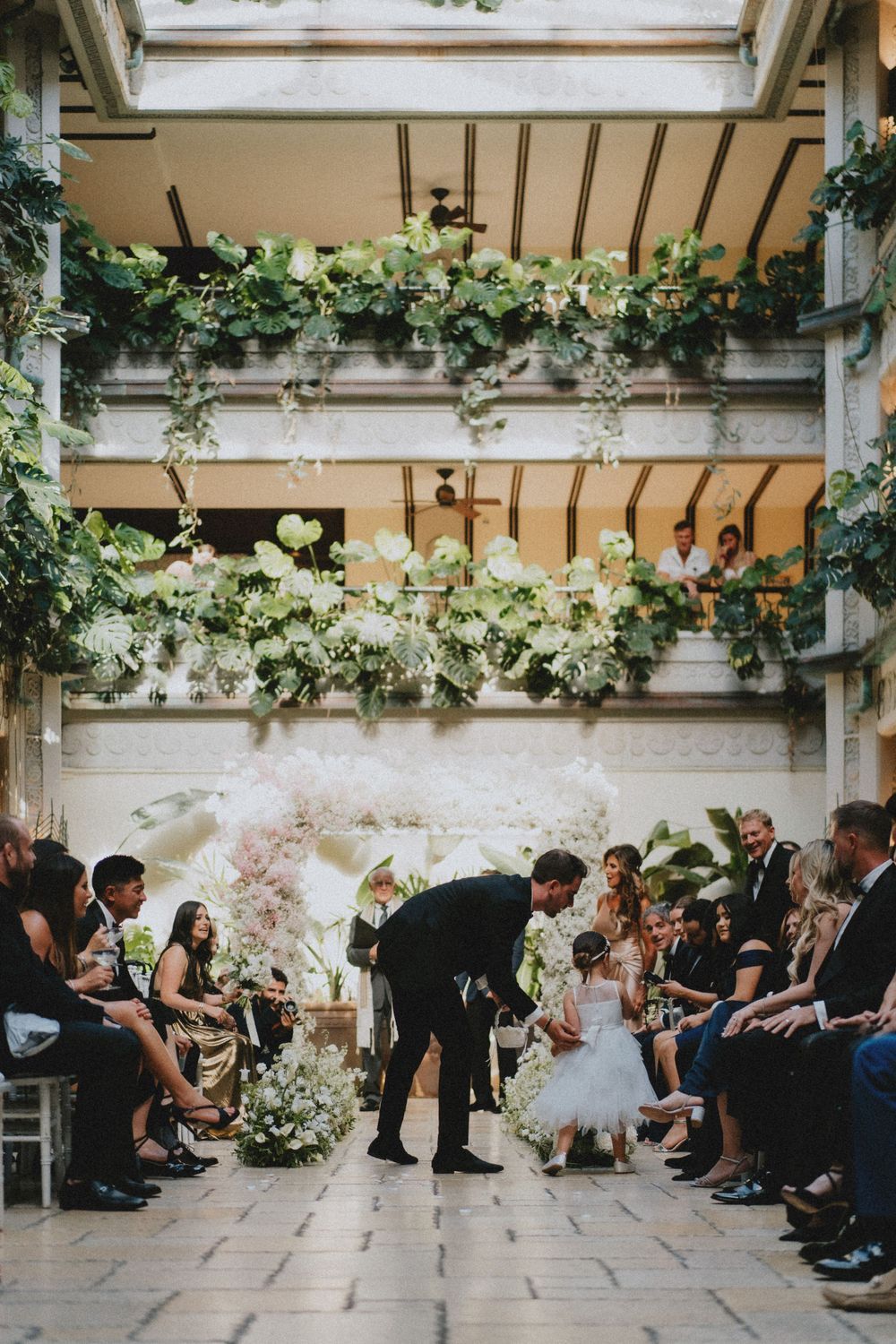 Indoor wedding ceremony space decorated with hanging greenery and white flowers.