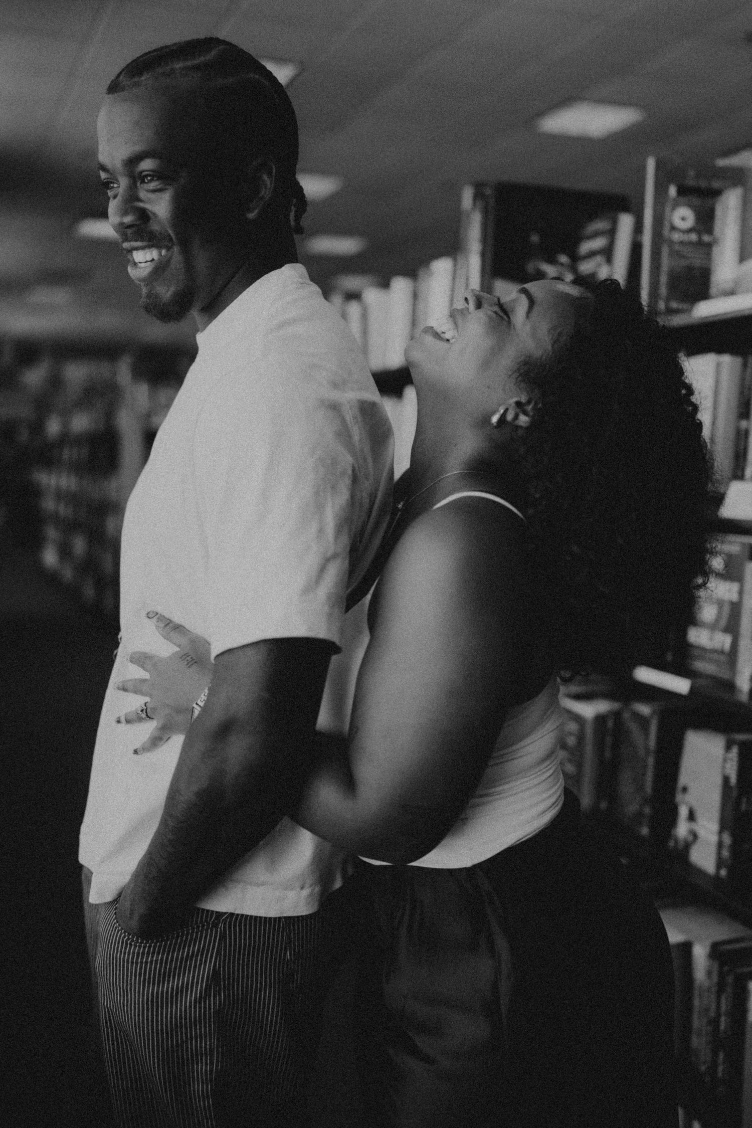 Joyful couple laughing together among bookshelves in black and white portrait.