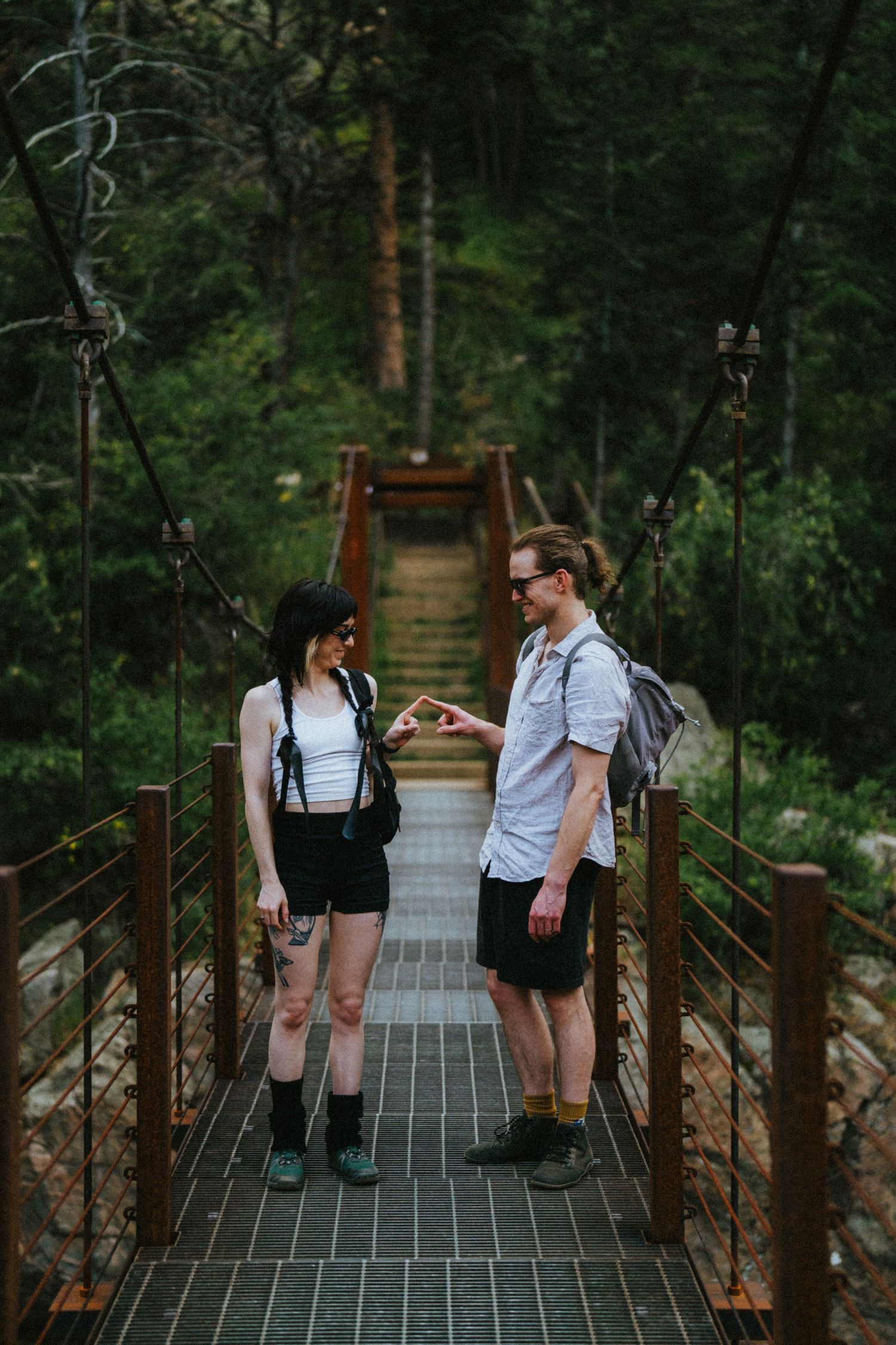 Couple fist bumping on a wooden suspension bridge surrounded by lush green forest during a hike.