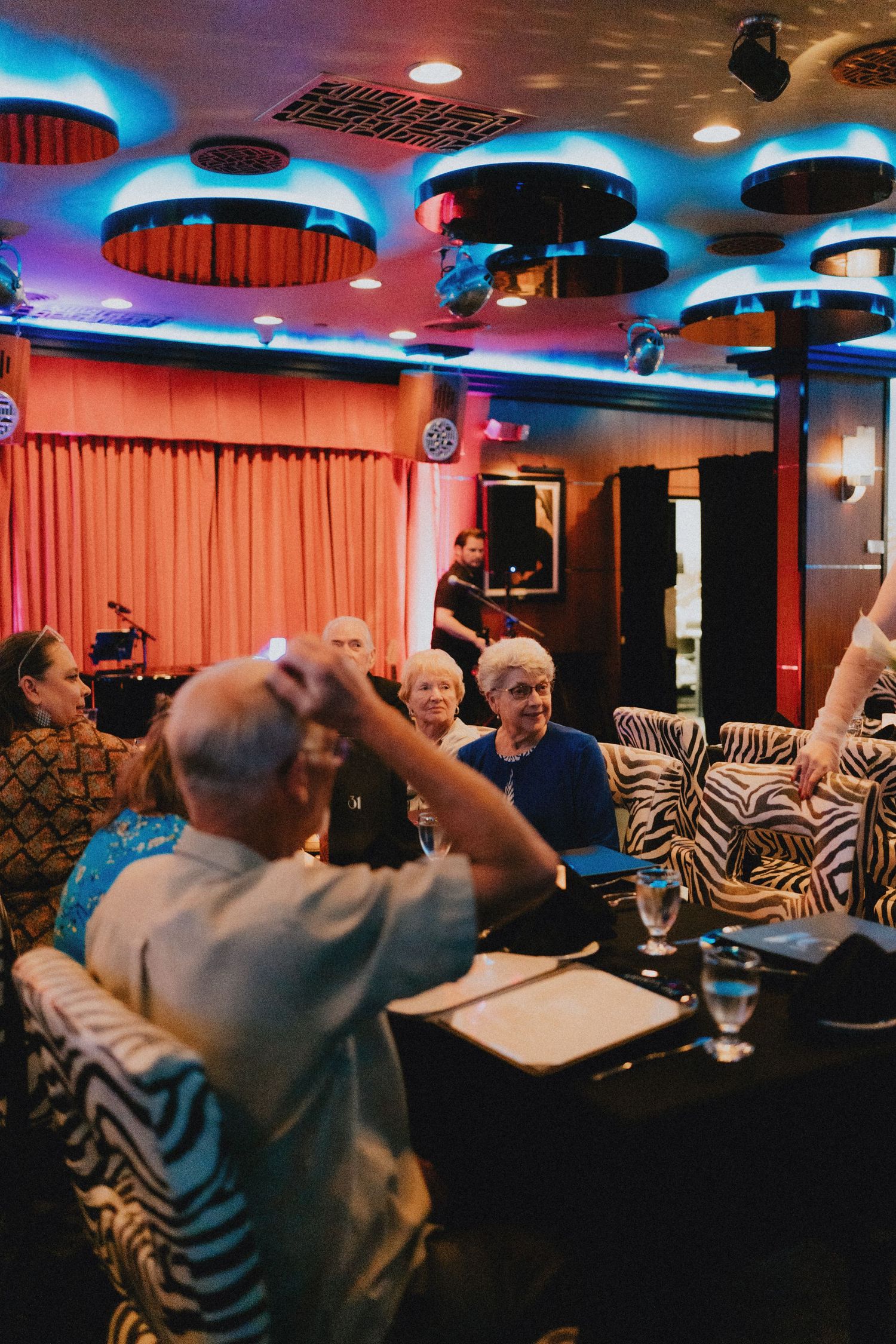 Wedding guests celebrate at a retro venue with zebra print chairs, colorful ceiling lights, and a live band performing.