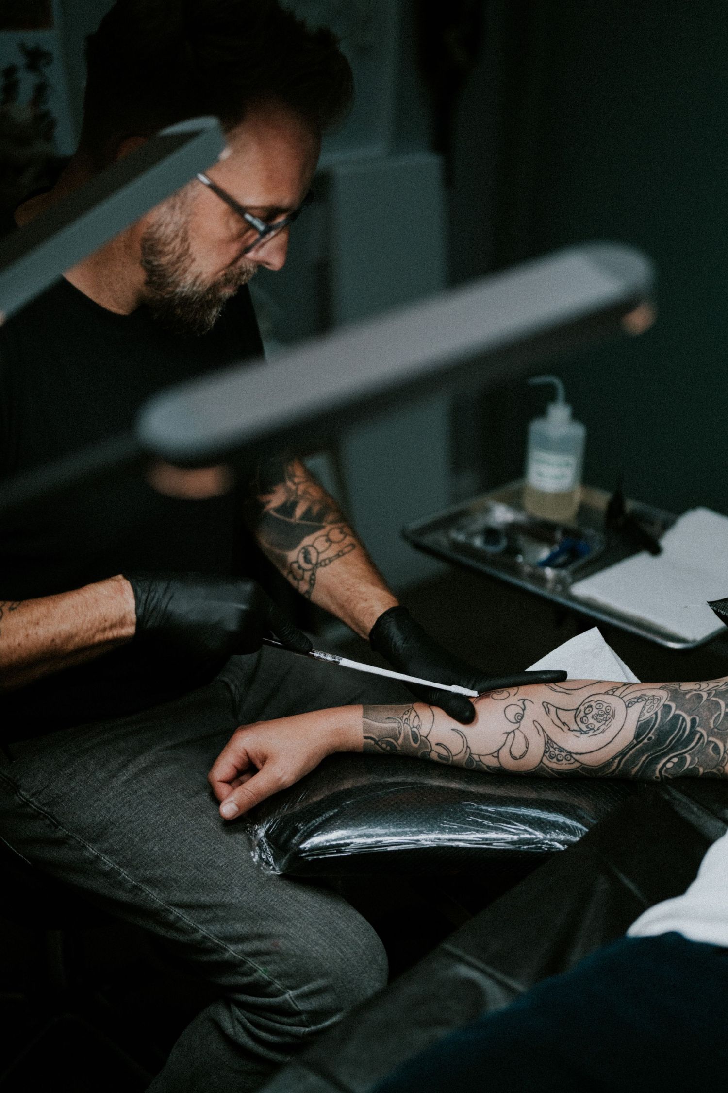 Closeup shots of tattooed arms preparing materials on a dark surface in moody lighting.