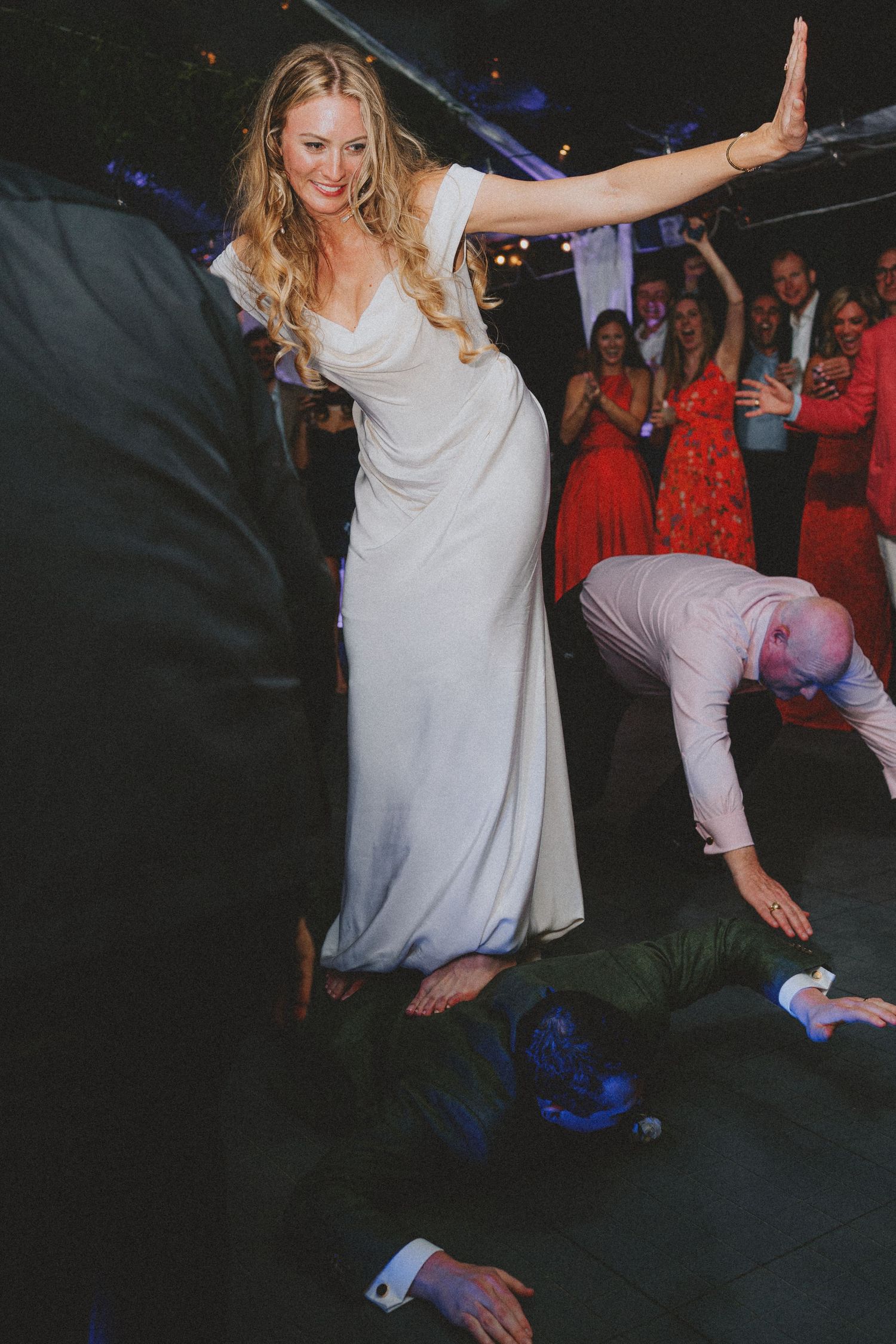 Bride in white gown dancing joyfully at wedding reception while guests cheer and celebrate on the dance floor.