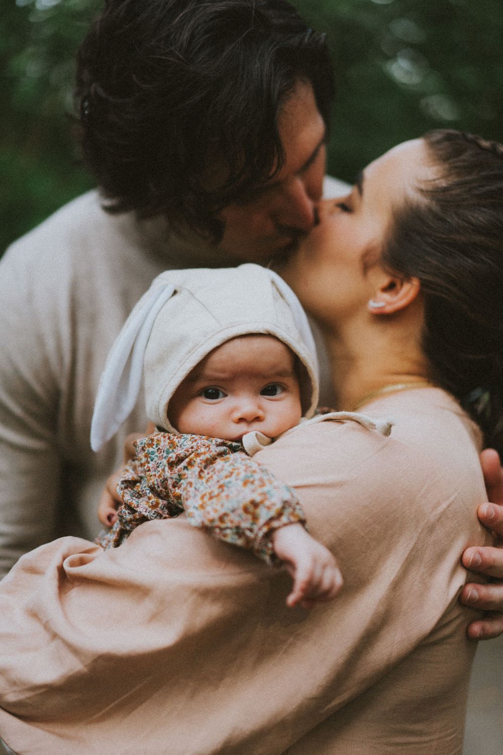 Intimate family moment captured in soft lighting as parent embraces small child in pink surroundings.