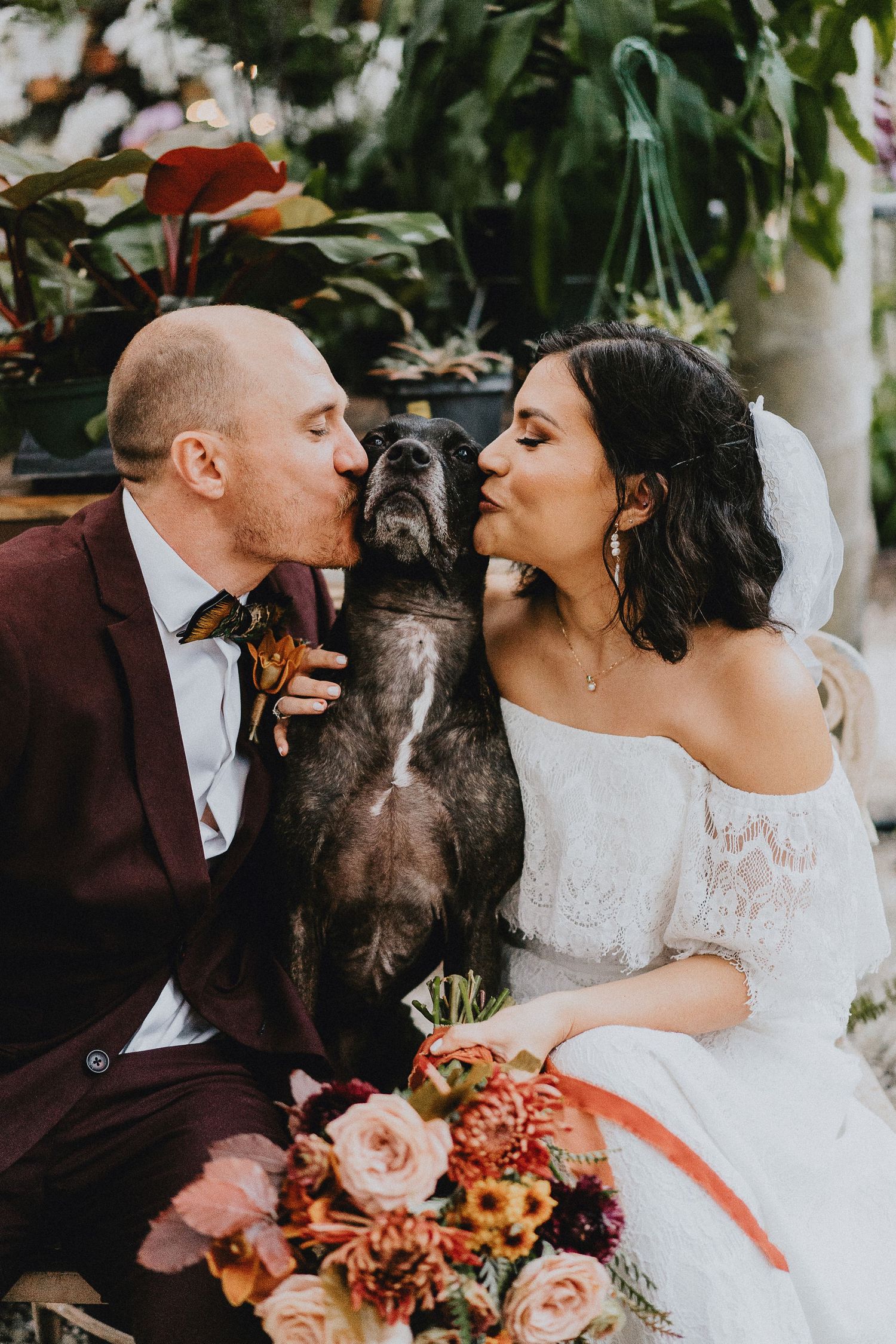 Couple poses with their dark dog for wedding photos surrounded by floral arrangements.