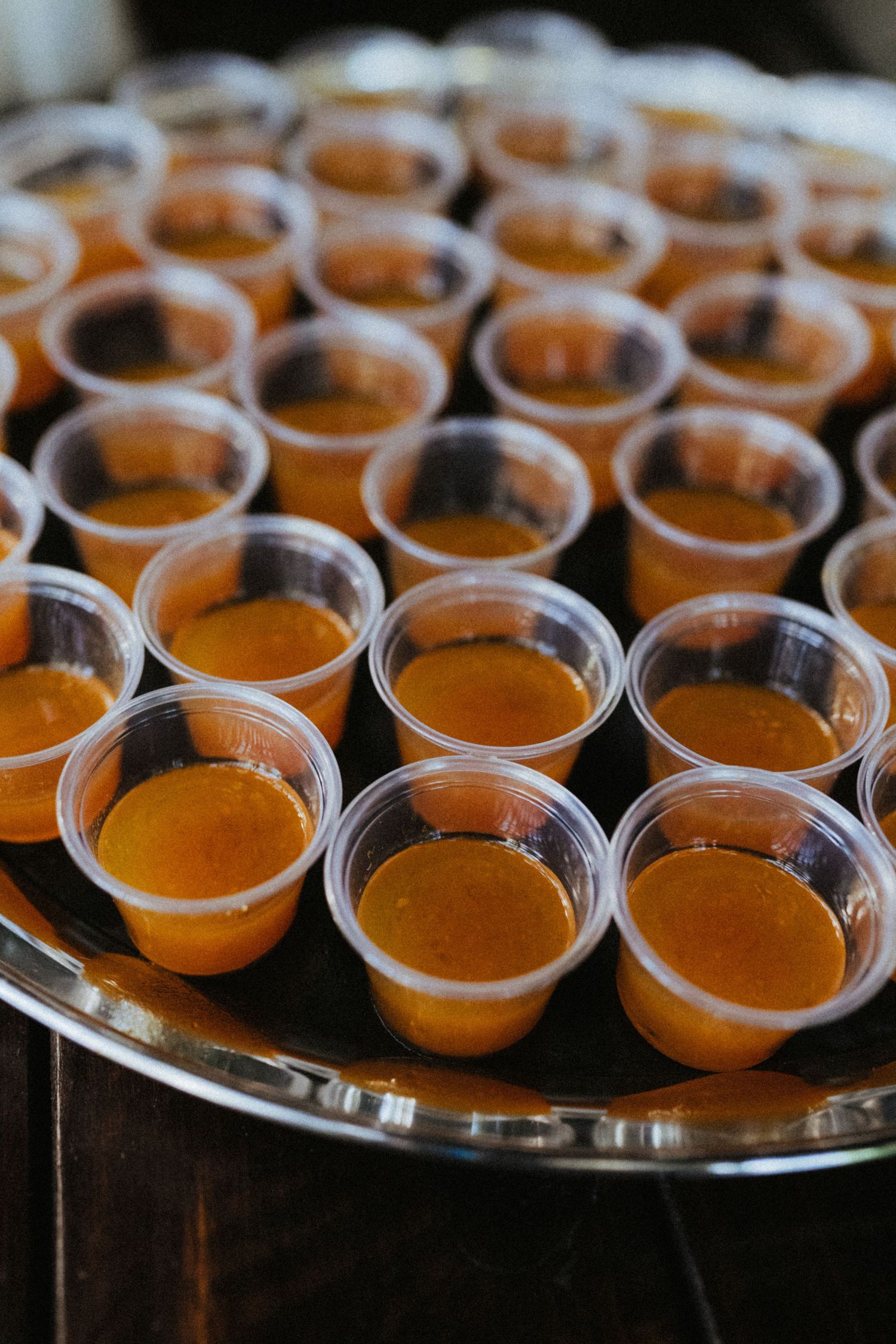 Tray of small plastic cups filled with orange juice or soup, arranged in rows on a silver serving platter.