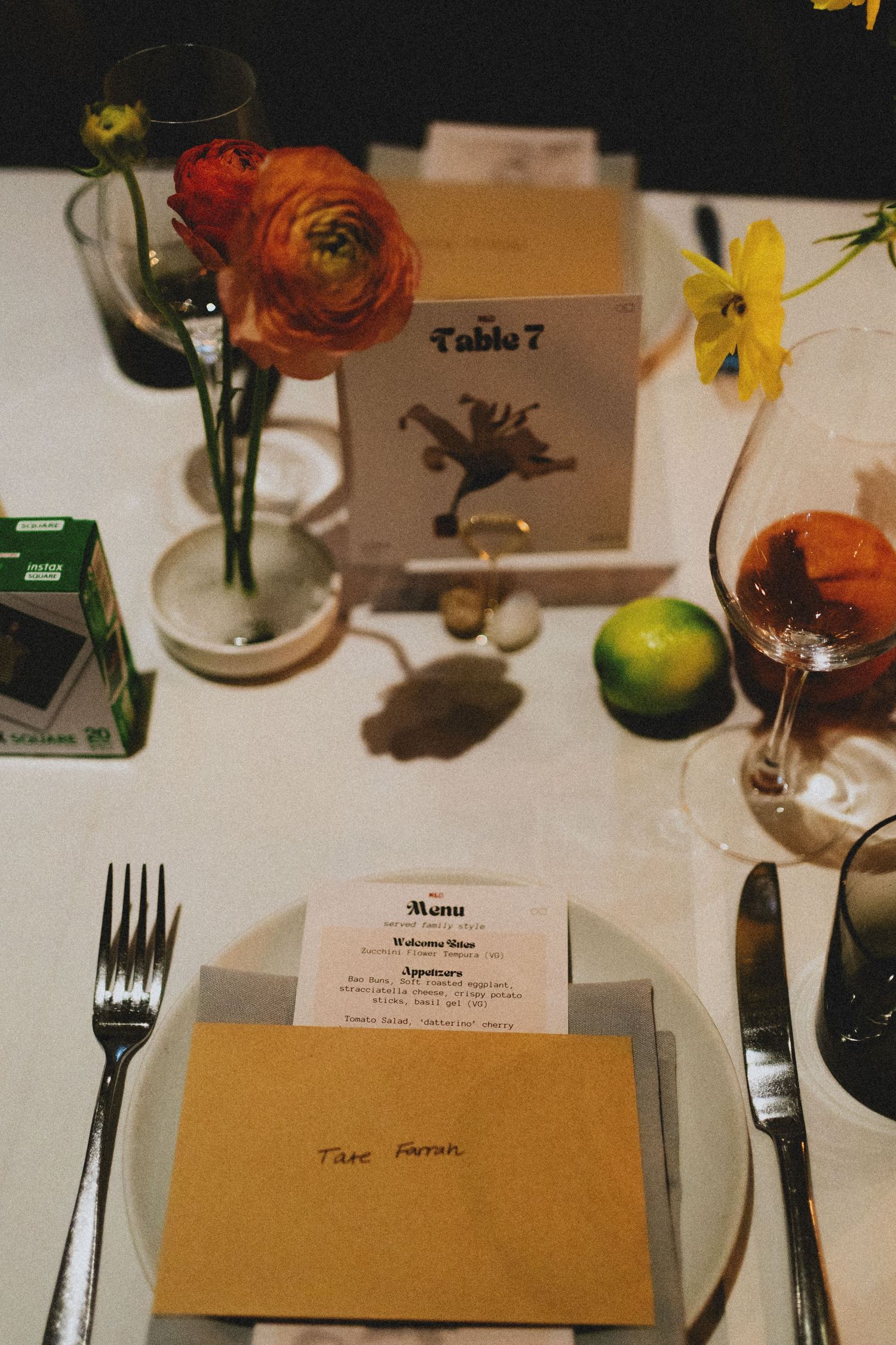 Table 7 place setting with menu card, ranunculus flowers, lime, and gold envelope at a formal dinner event.