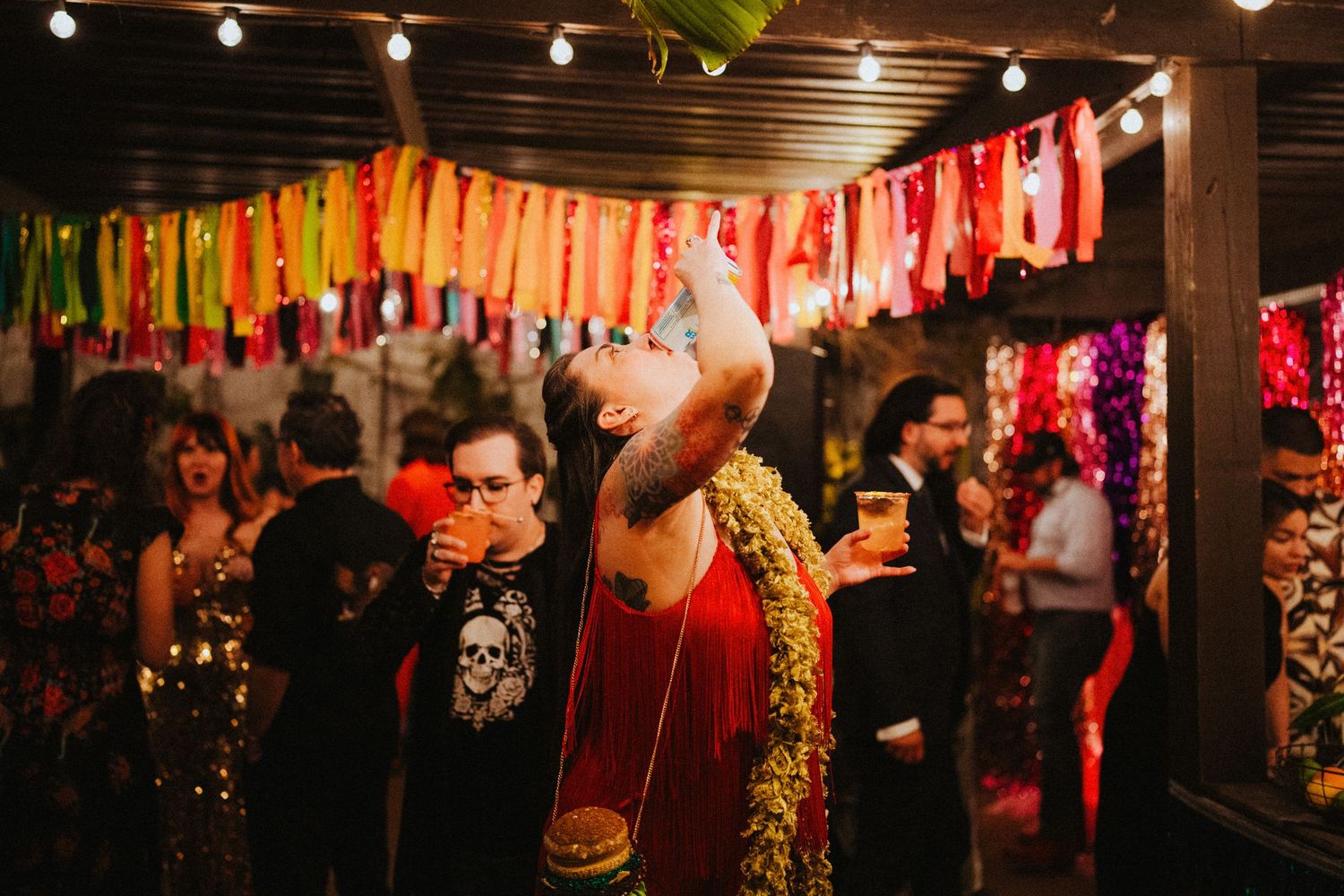 Man drinking at colorful party with vibrant ribbon garlands and festive decorations hanging overhead.