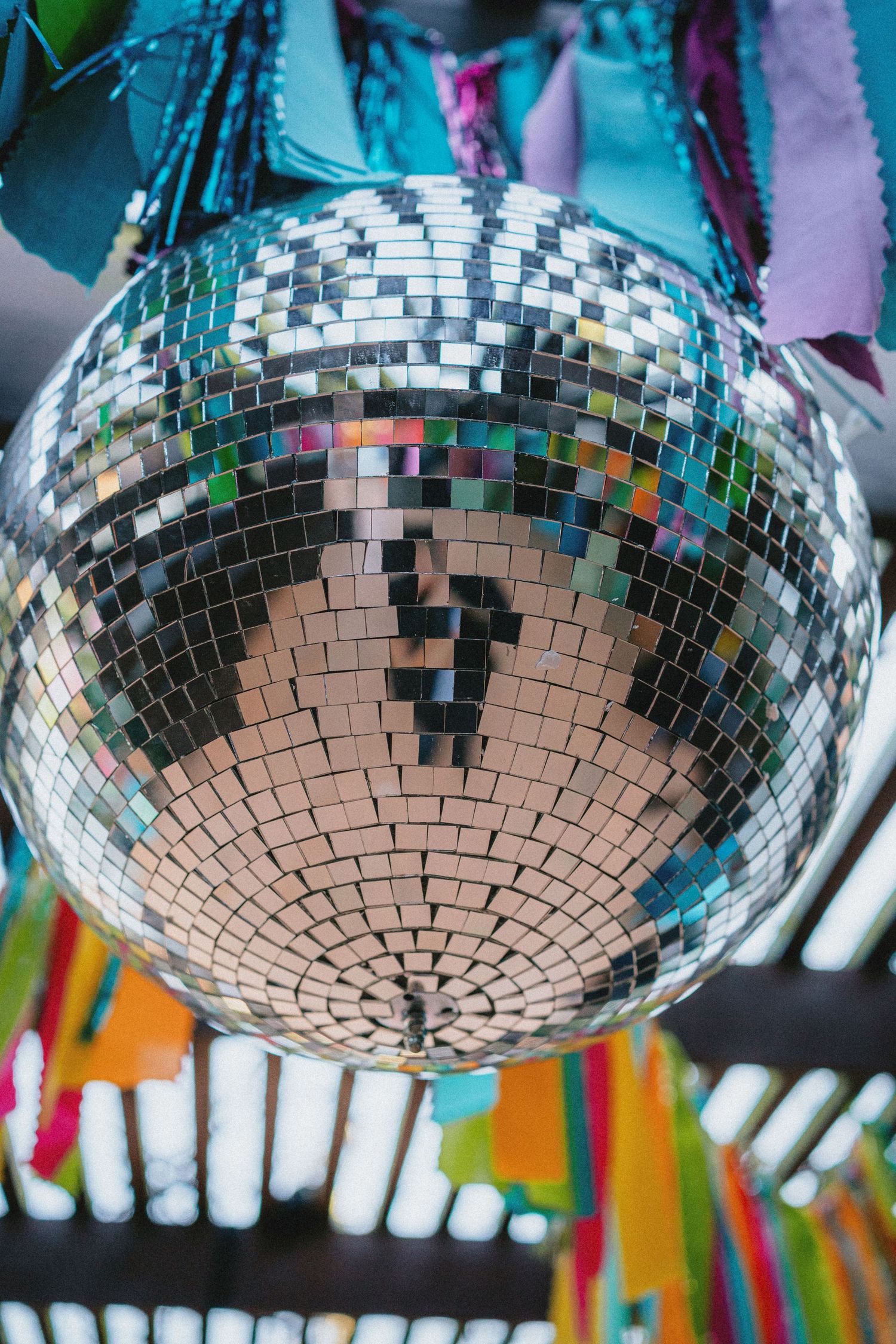 A shiny silver disco ball with colorful ribbons hanging from the ceiling at a festive party event.