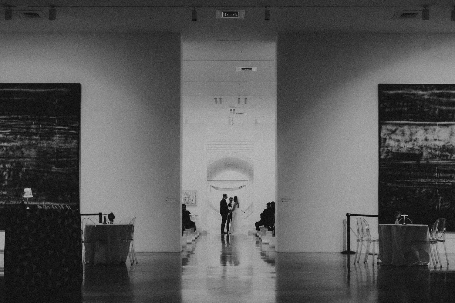 Black and white photo of couple silhouetted in elegant museum gallery hallway with large art pieces.