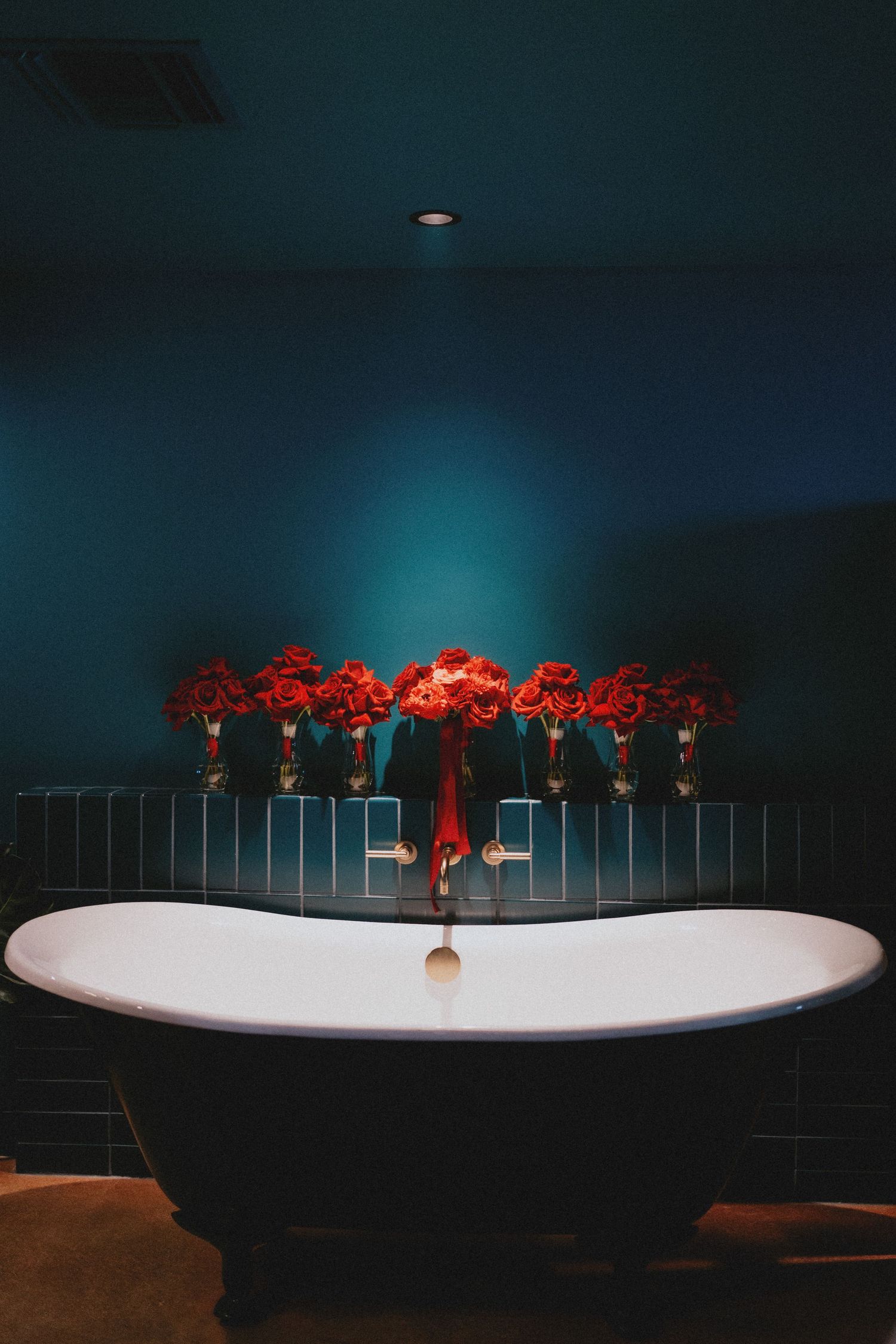 A modern bathroom interior featuring red flowers displayed above a freestanding bathtub with dramatic lighting.