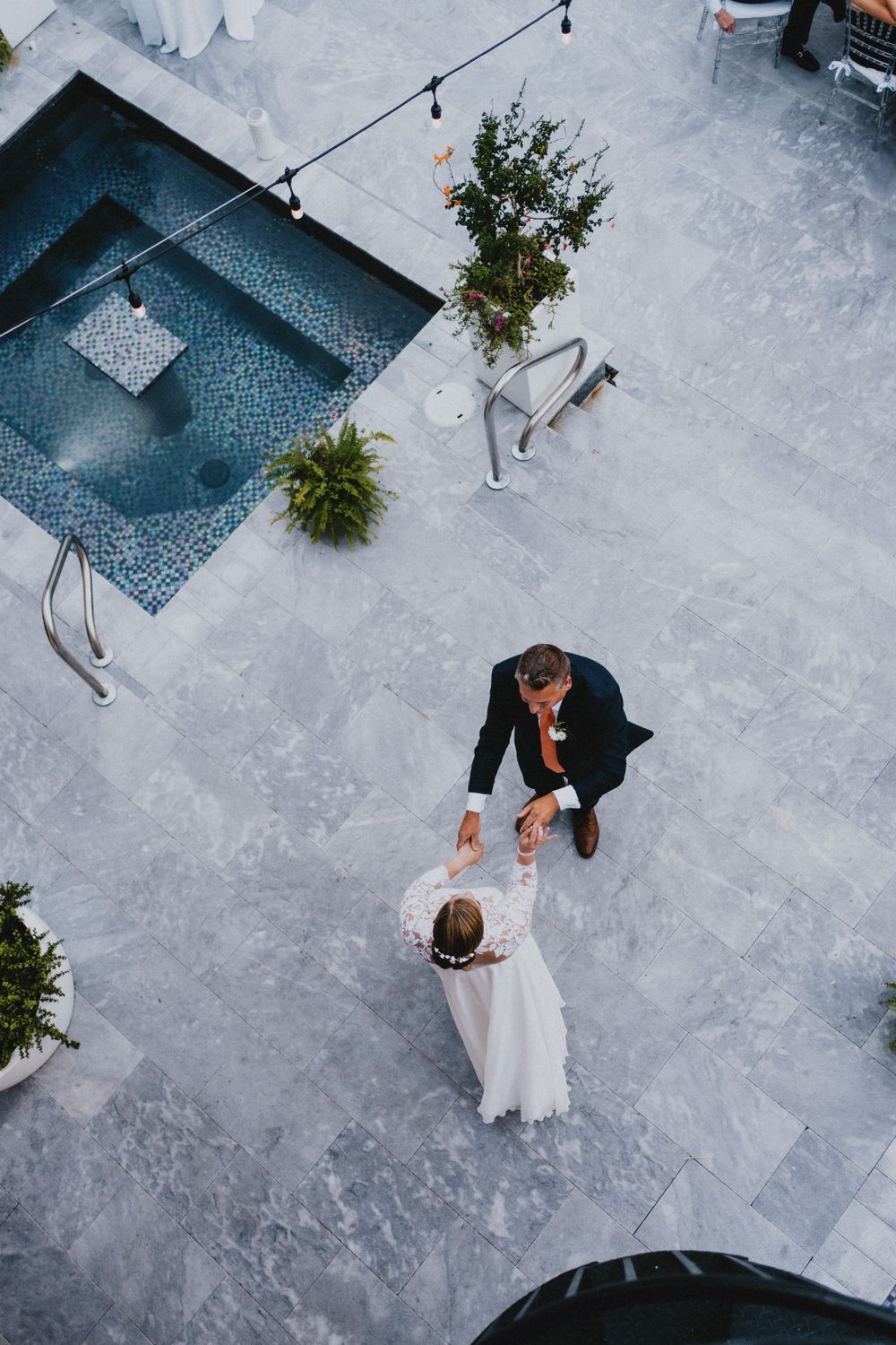 Aerial view of a couple dancing on a white marble patio near a decorative pool.