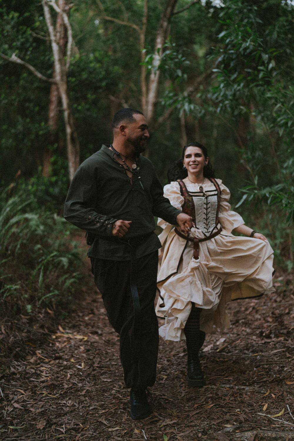 A couple in contrasting outfits dancing together in a wooded forest setting.