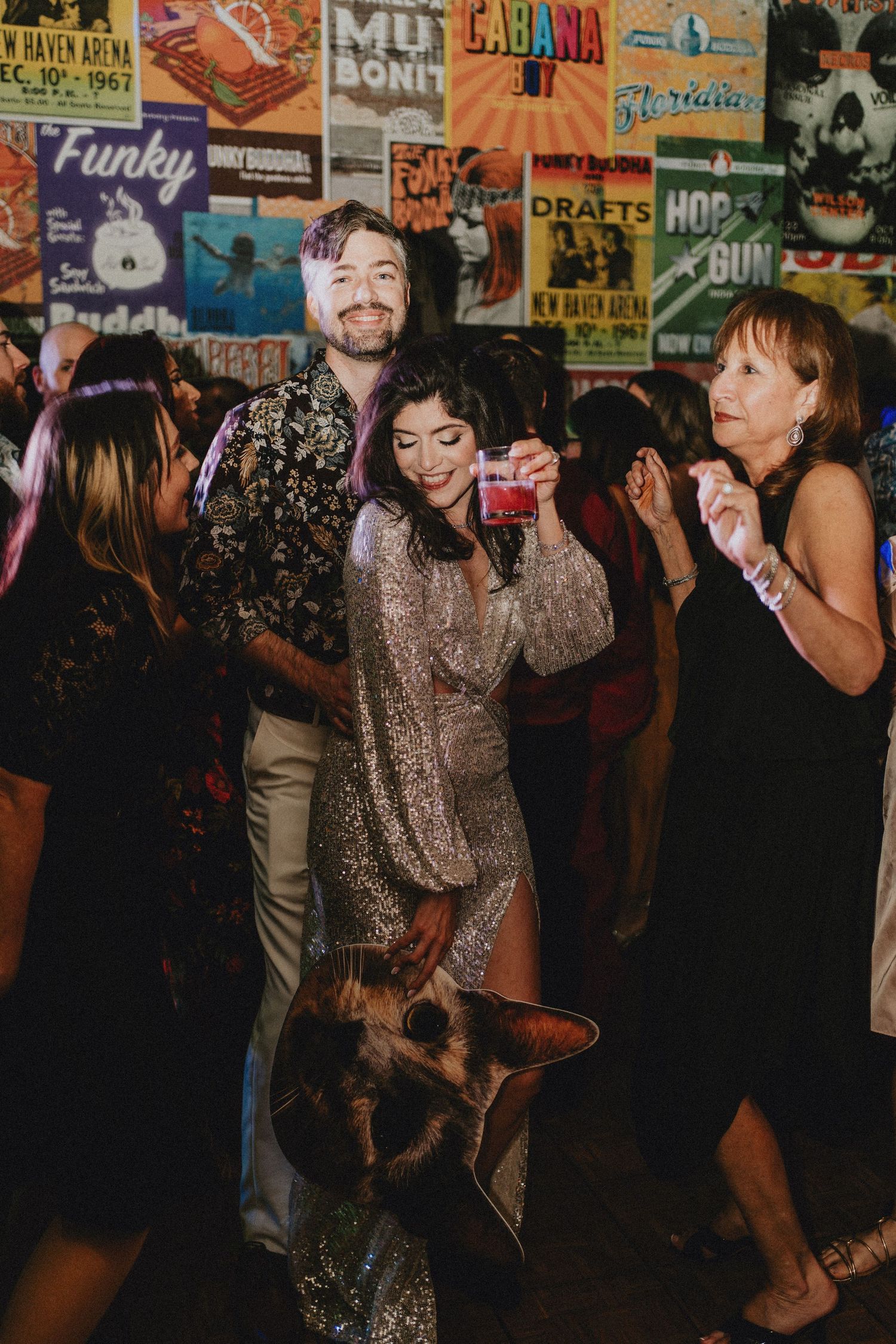 Couple dancing at a lively party with colorful vintage posters on the wall behind them.