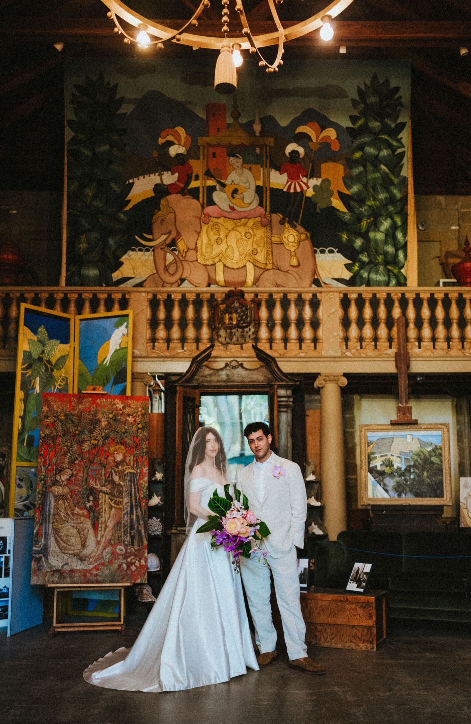 Bride and groom pose in an art gallery wedding venue surrounded by colorful paintings and ornate decor.