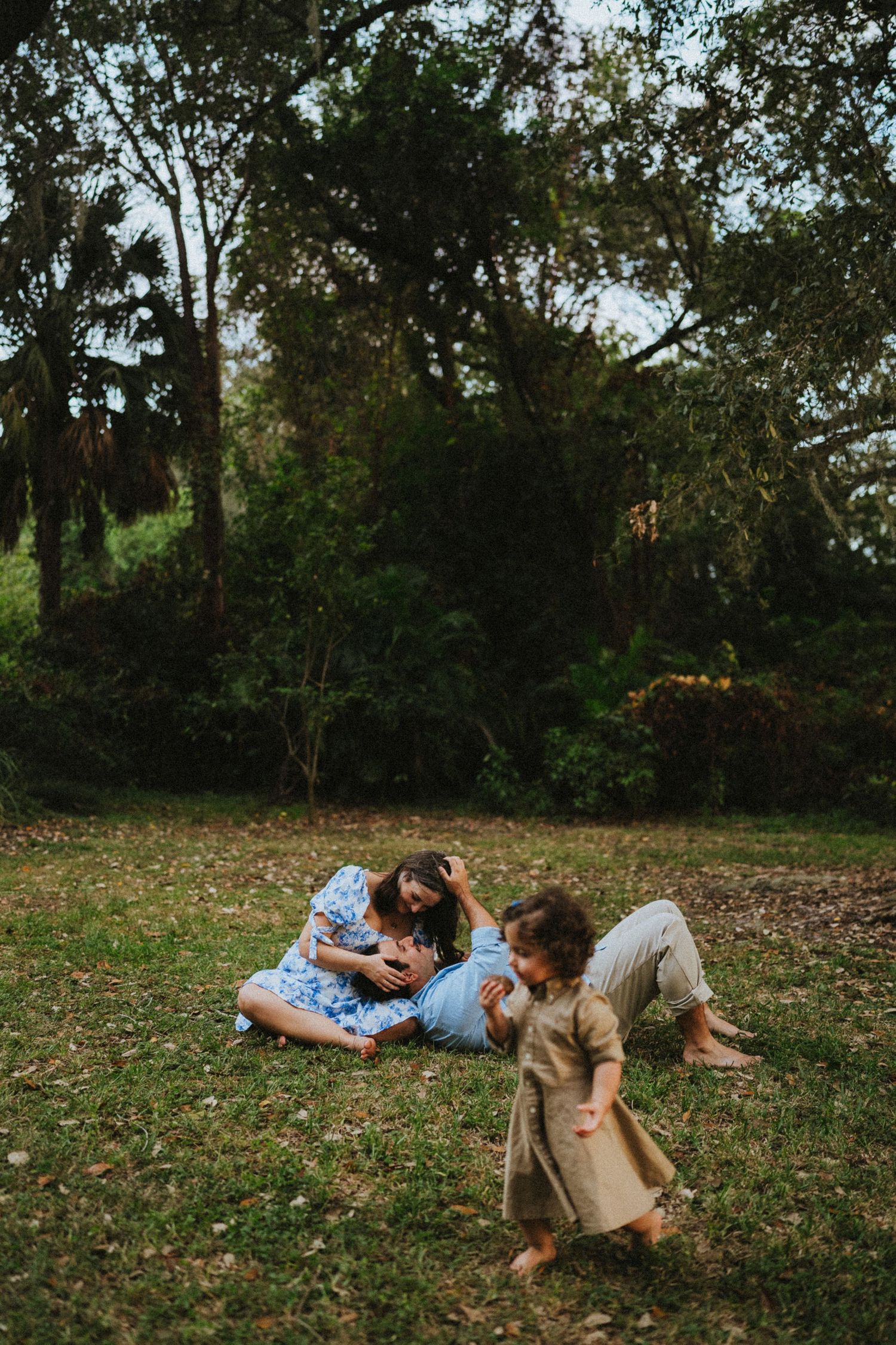 A family relaxes together on grass in a wooded area during a warm afternoon.