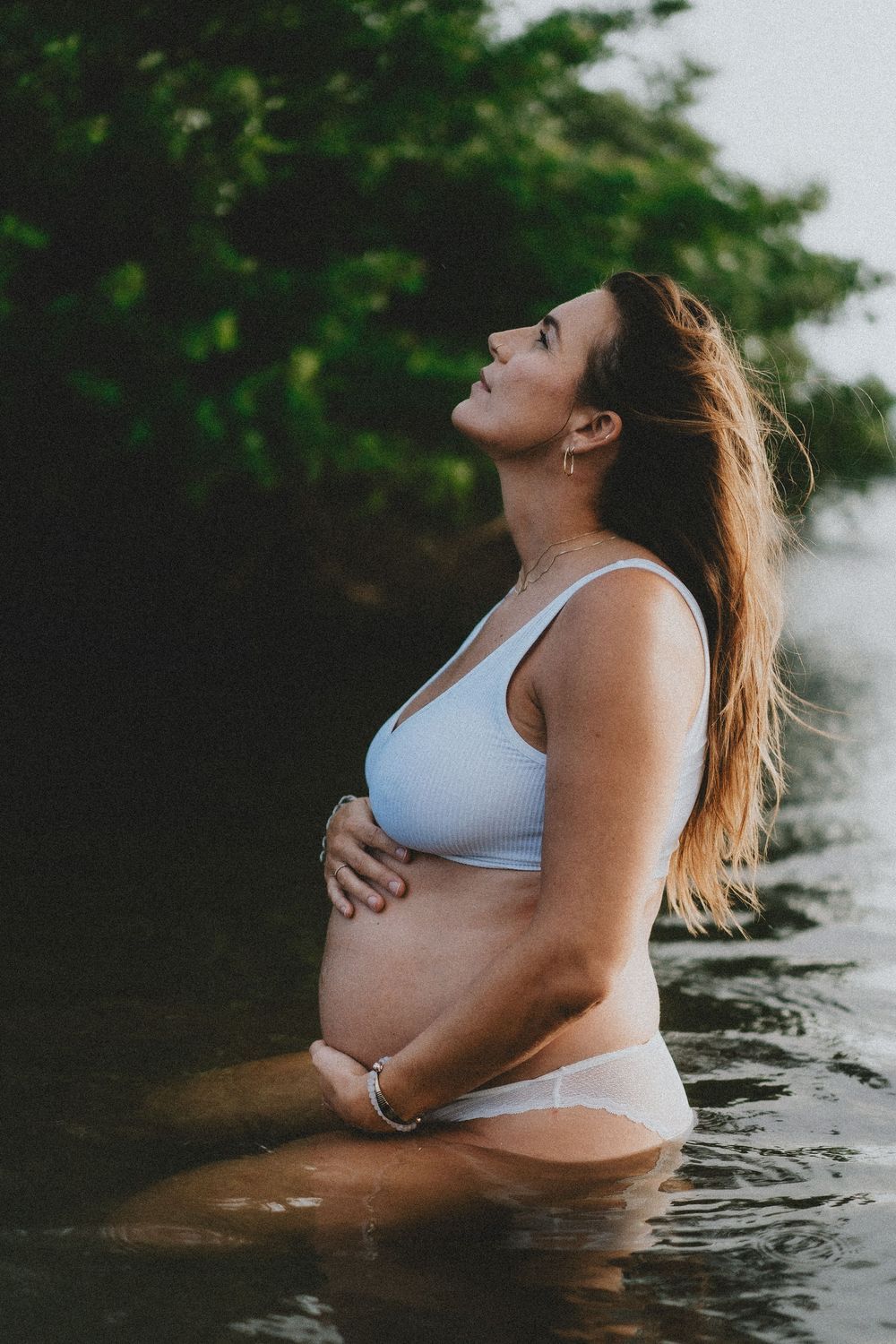 Intimate maternity photography of an expectant mother in water during sunset or sunrise.