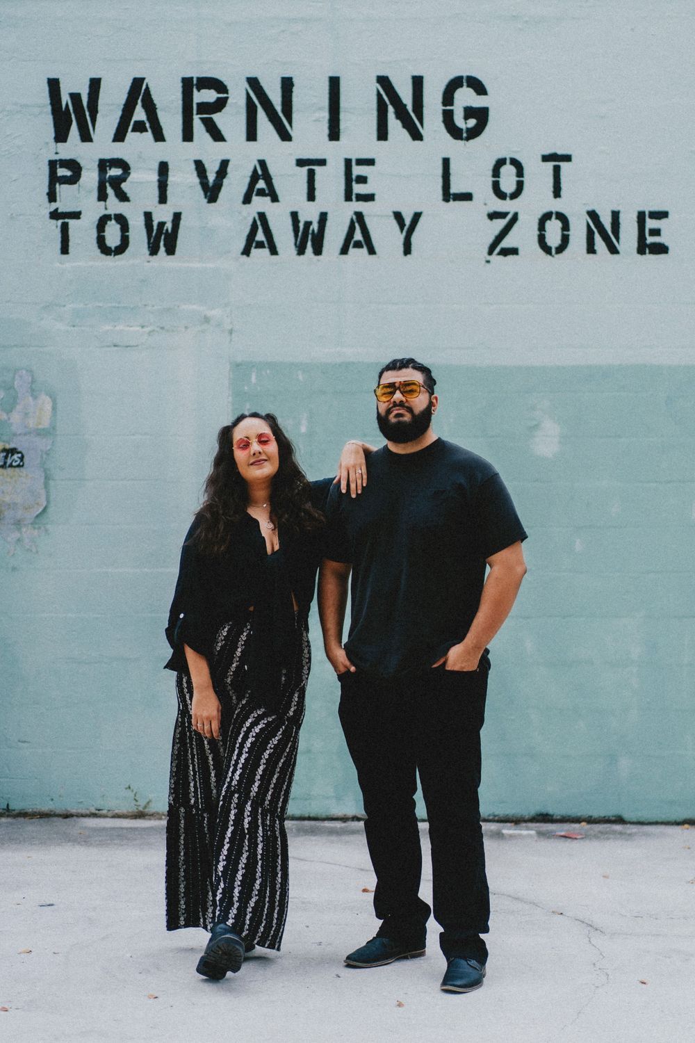 Couple posing against blue wall with warning sign text in urban setting.