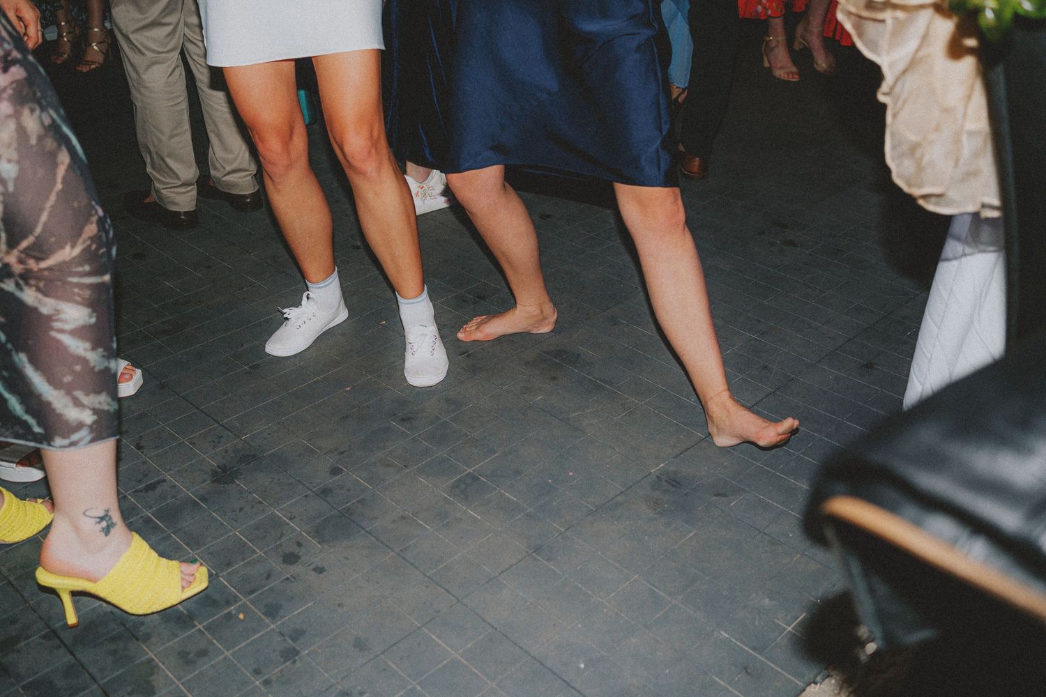 Close-up of guests dancing barefoot and in socks on a tiled floor at a wedding reception.