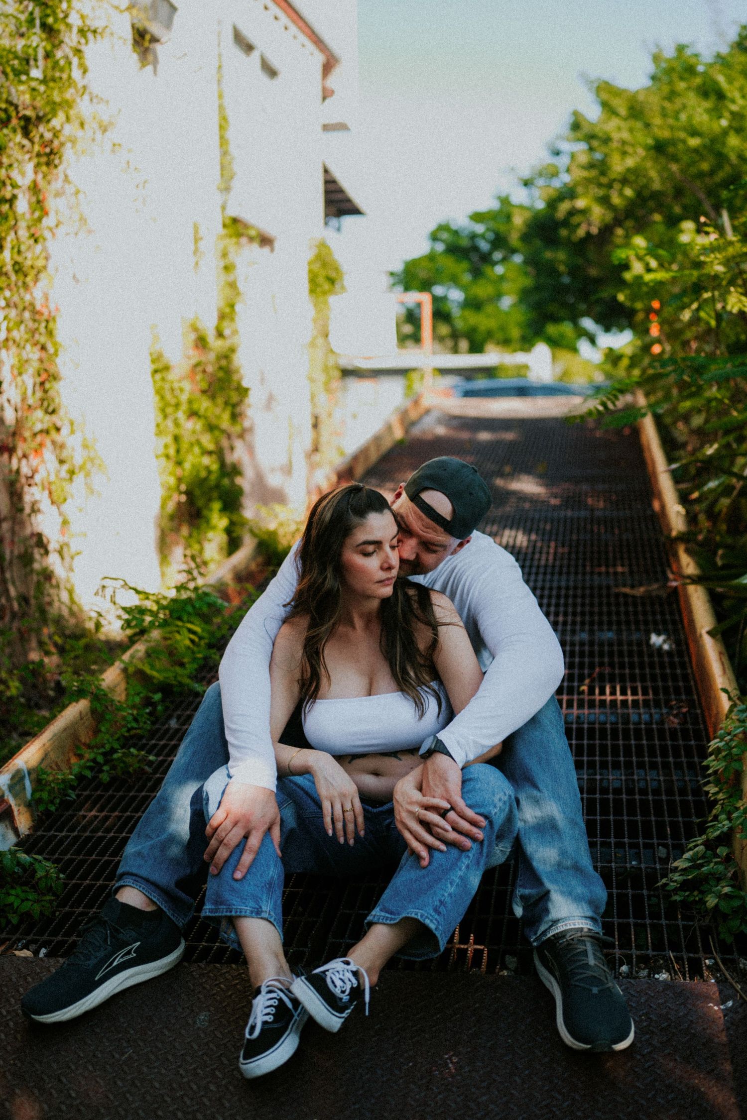 A couple sitting on outdoor steps together at sunset in casual denim and sneakers.