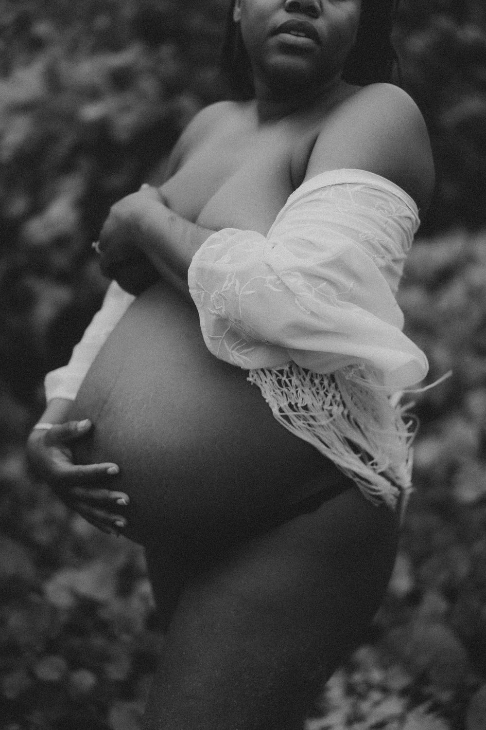 Artistic black and white maternity photo showing a pregnant belly with flowing white fabric against a natural background.