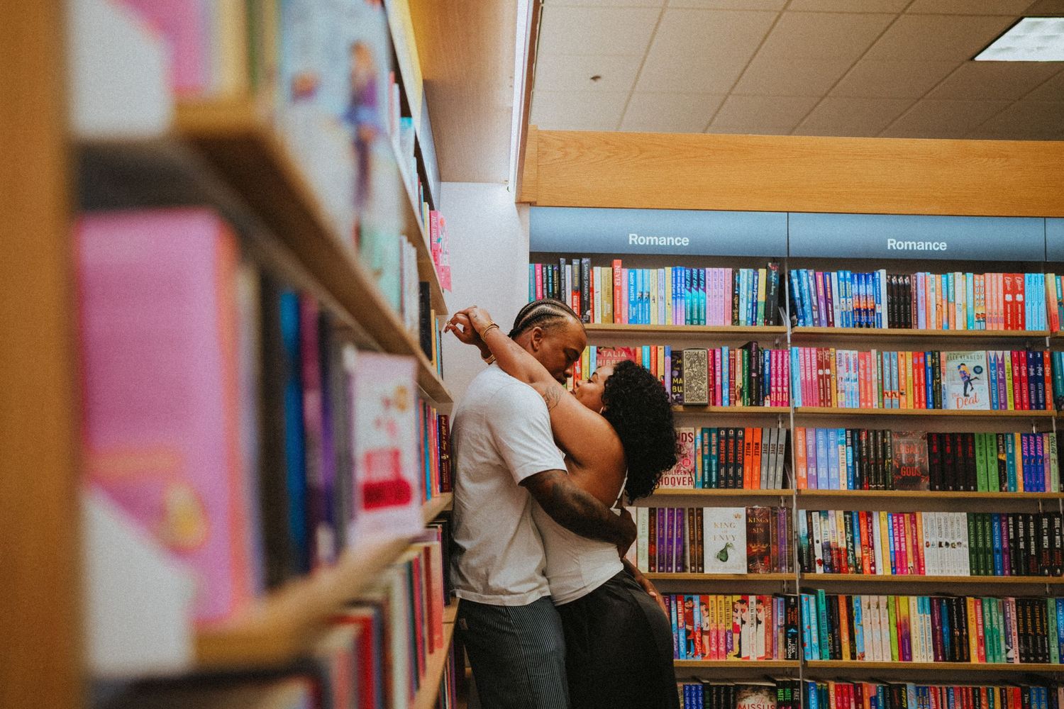 Couple sharing a romantic kiss between colorful bookshelves in a cozy bookstore.