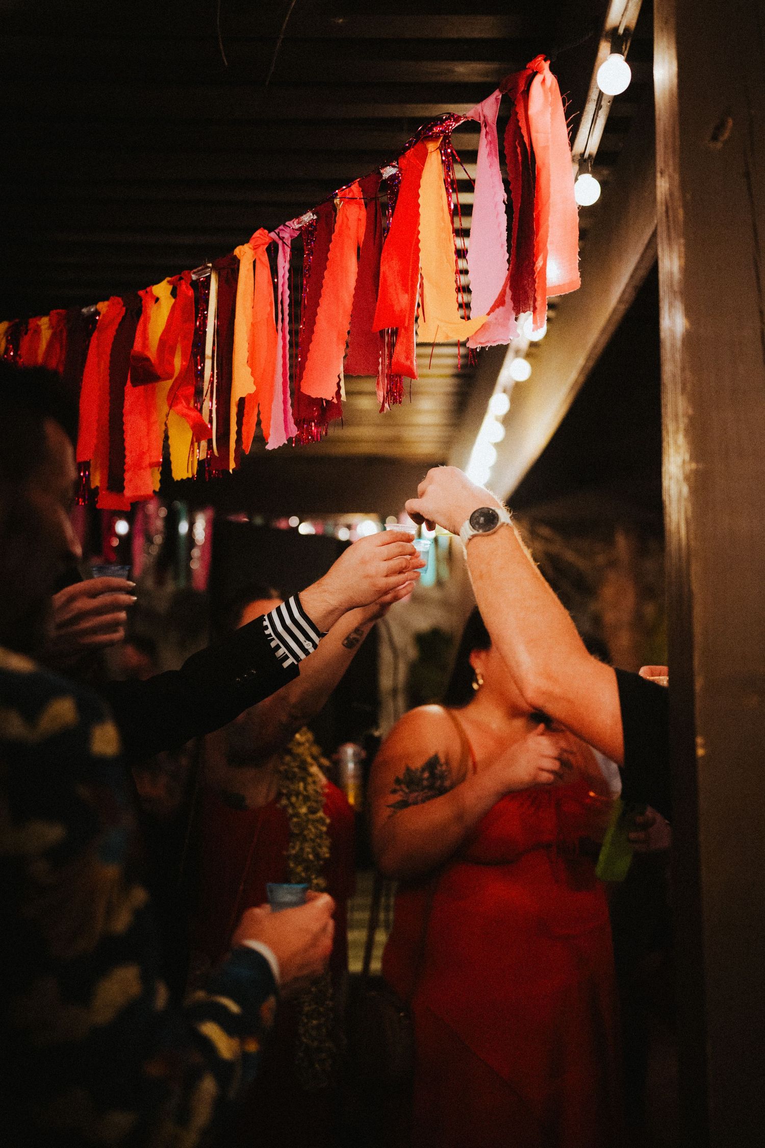 People celebrating at a party under colorful red fabric garland decorations with string lights at night.