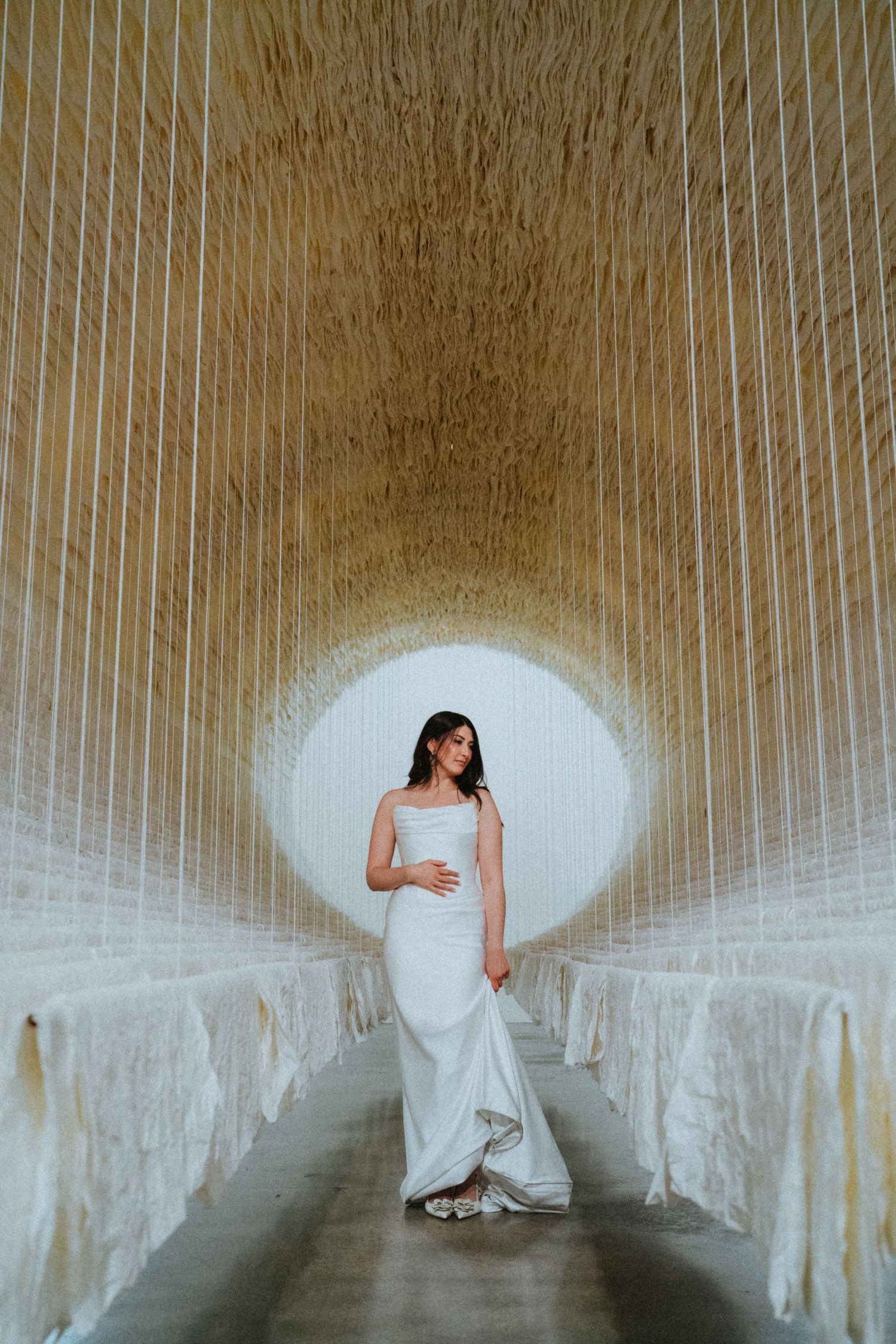 Bride in white gown stands in golden tunnel corridor with circular glowing backdrop at wedding venue.