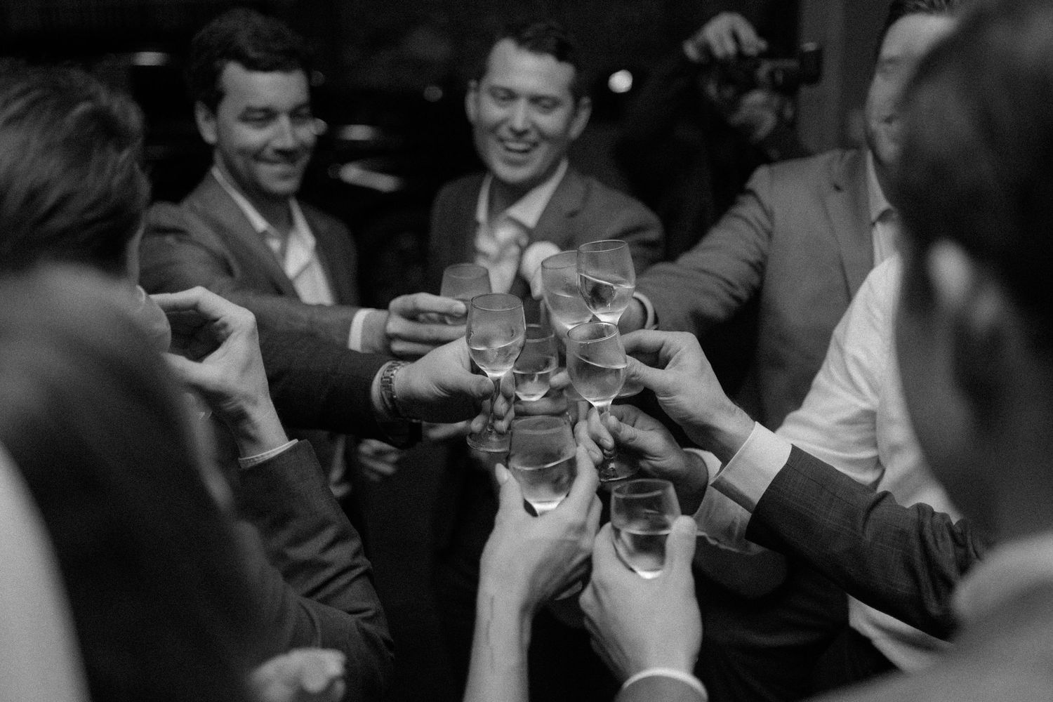 Black and white photo of a group of men in suits toasting with champagne glasses at a celebration.