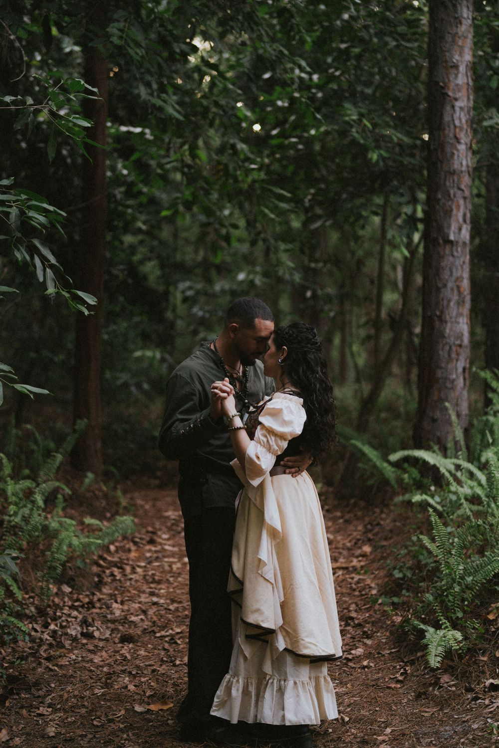 A couple shares an intimate dance among tall trees on a forest path.