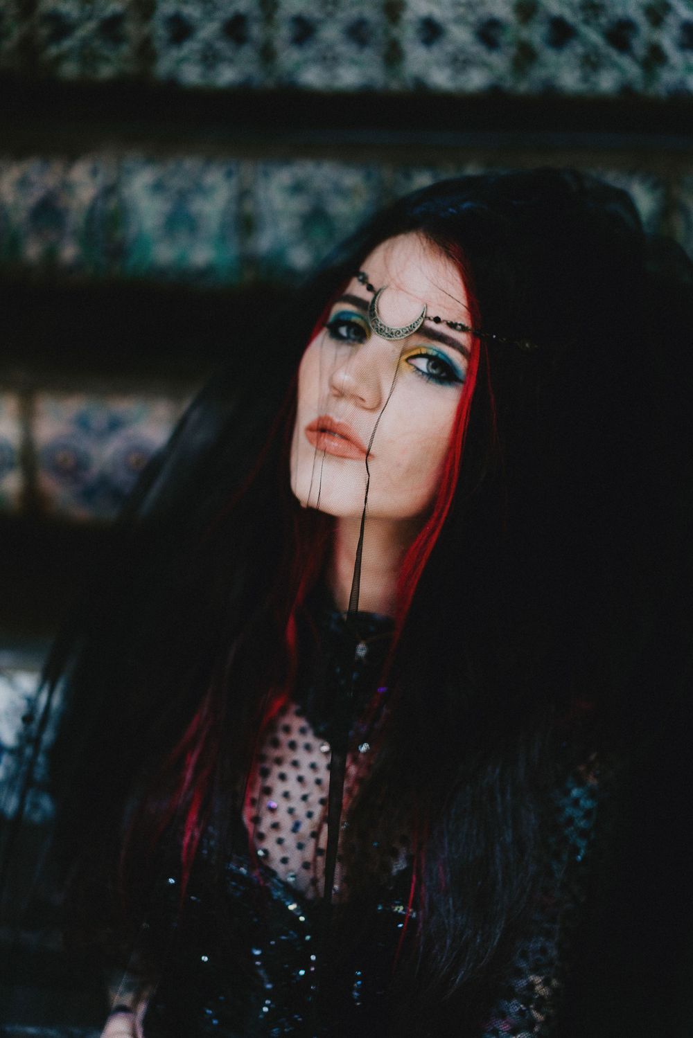Gothic fashion portrait with red highlights against patterned dark background.