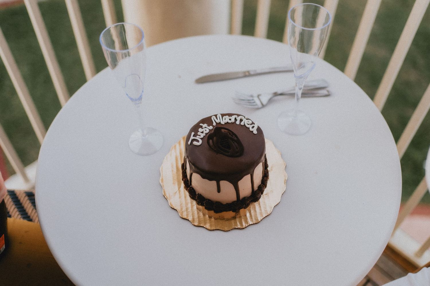Small chocolate wedding cake reading Just Married on white table with champagne flutes.