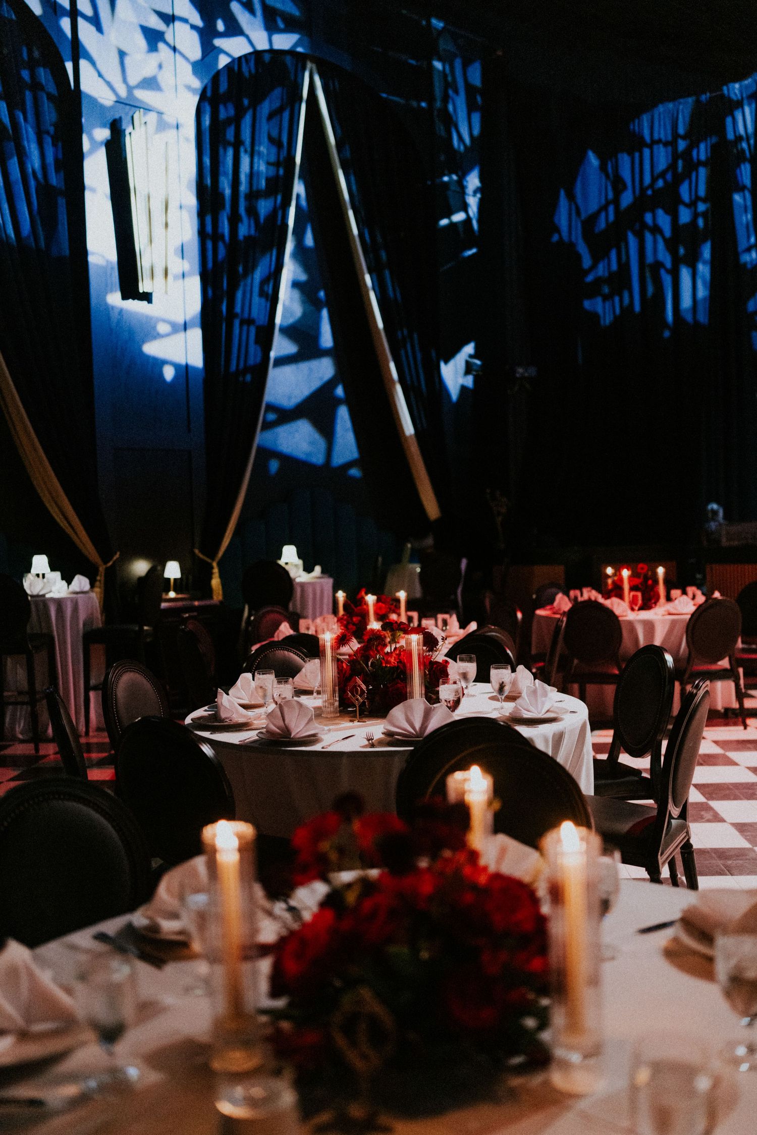 Elegant candlelit wedding reception with red floral centerpieces, white tablecloths, and dramatic blue lighting.