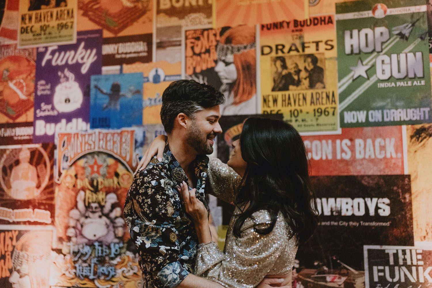 Couple sharing a romantic moment in front of colorful vintage concert posters at a funky bar venue.