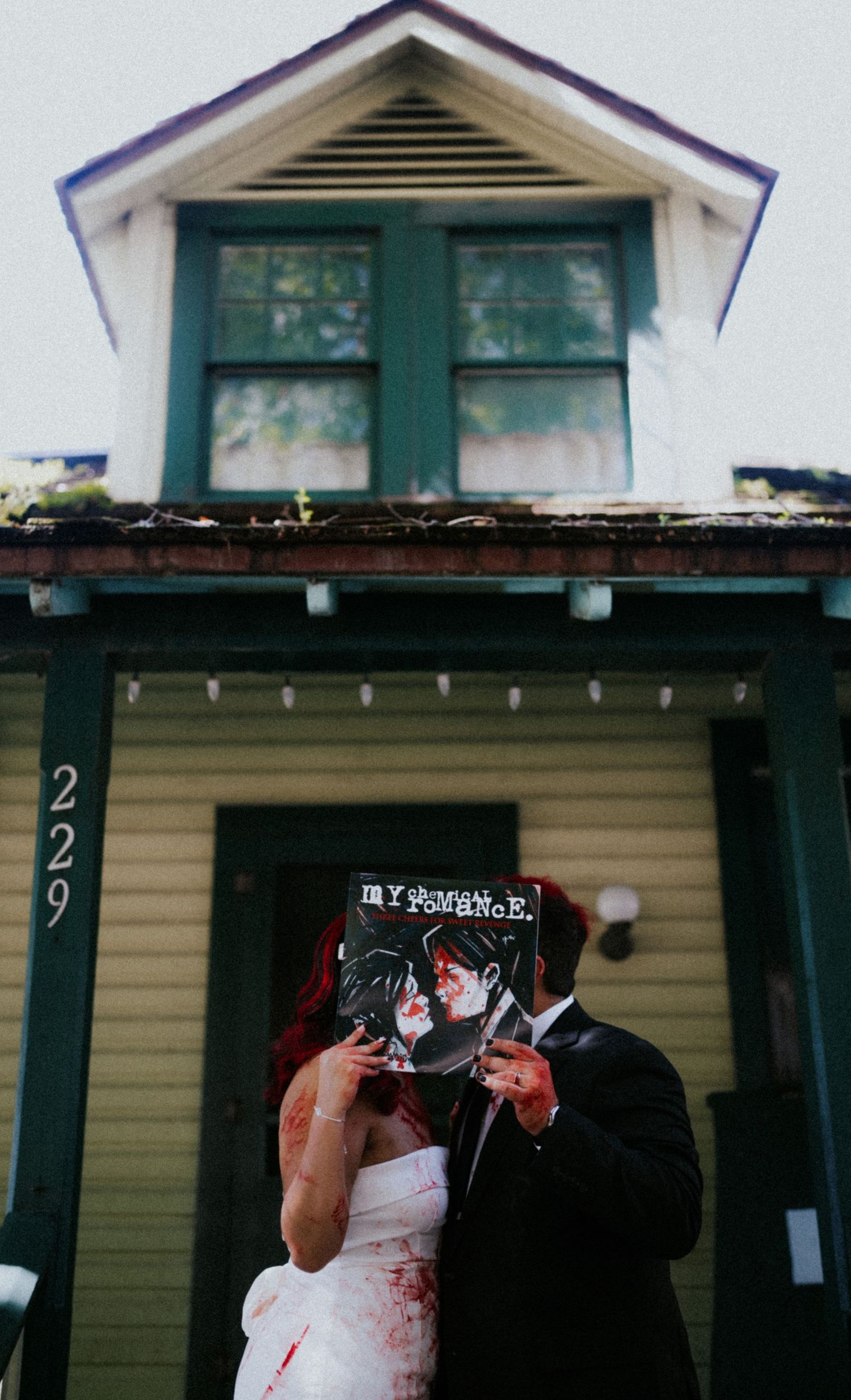Zombie bride and groom holding My Chemical Romance album cover outside house number 229 at Halloween wedding.