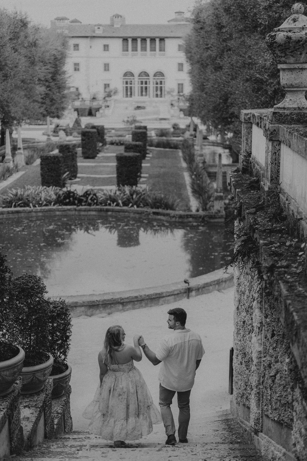 A vintage black and white photograph shows two people walking along a grand estate pathway.