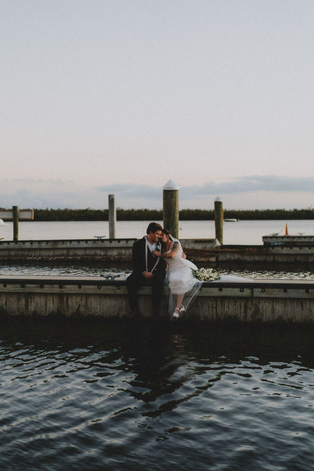 Couple sitting on waterfront dock during sunset with ocean view.