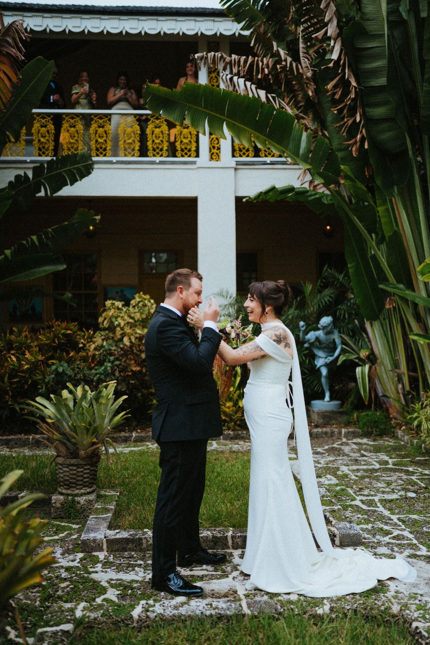 Bride and groom share a tender first look moment in a lush tropical garden courtyard during their wedding day.