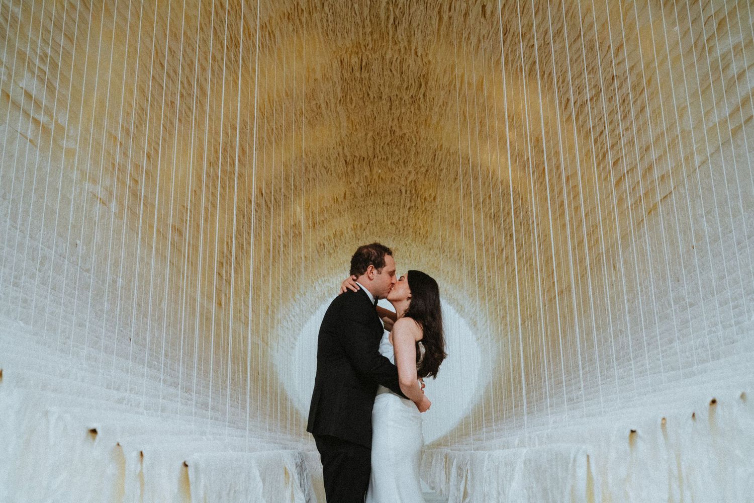 Couple sharing a romantic kiss in a stunning golden tunnel wedding venue with elegant draping decor.