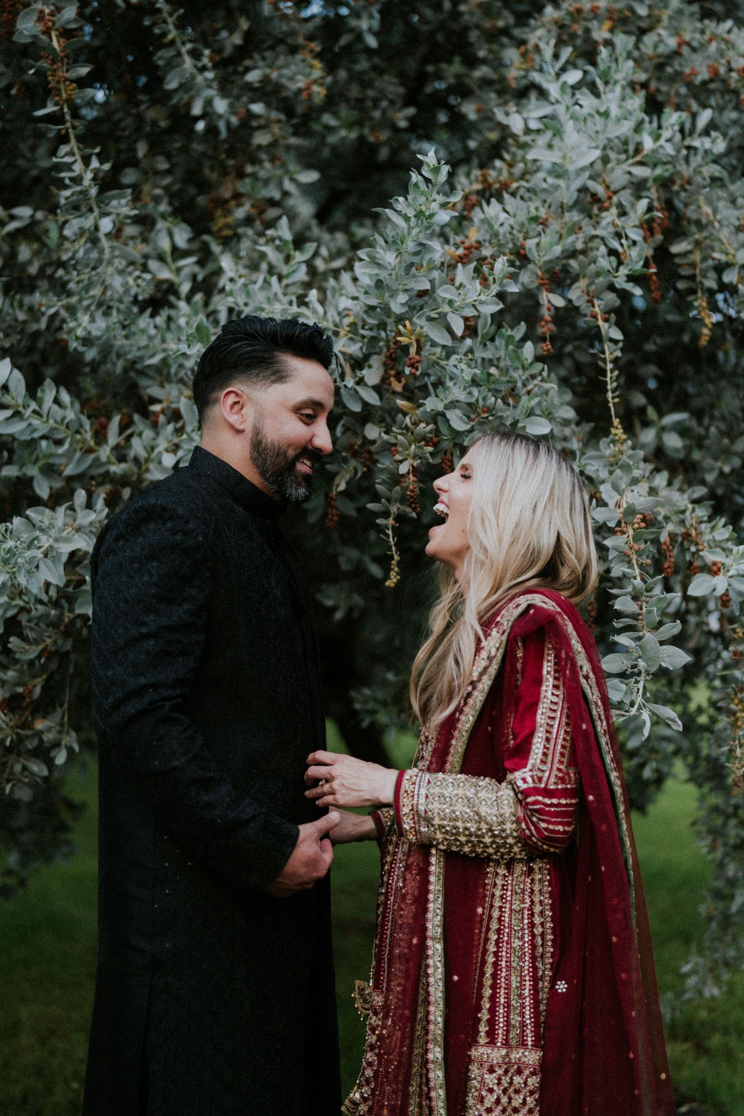 A couple in traditional South Asian wedding attire share intimate moments in a garden setting.