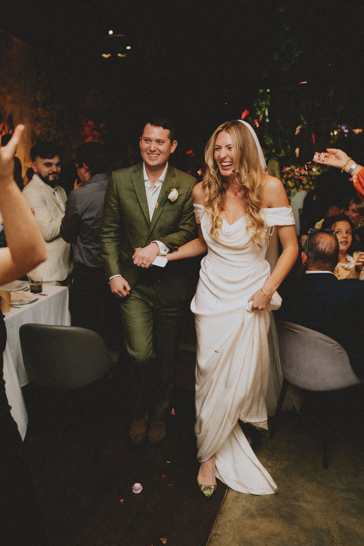 Newlyweds joyfully entering wedding reception hall with guests celebrating around them.