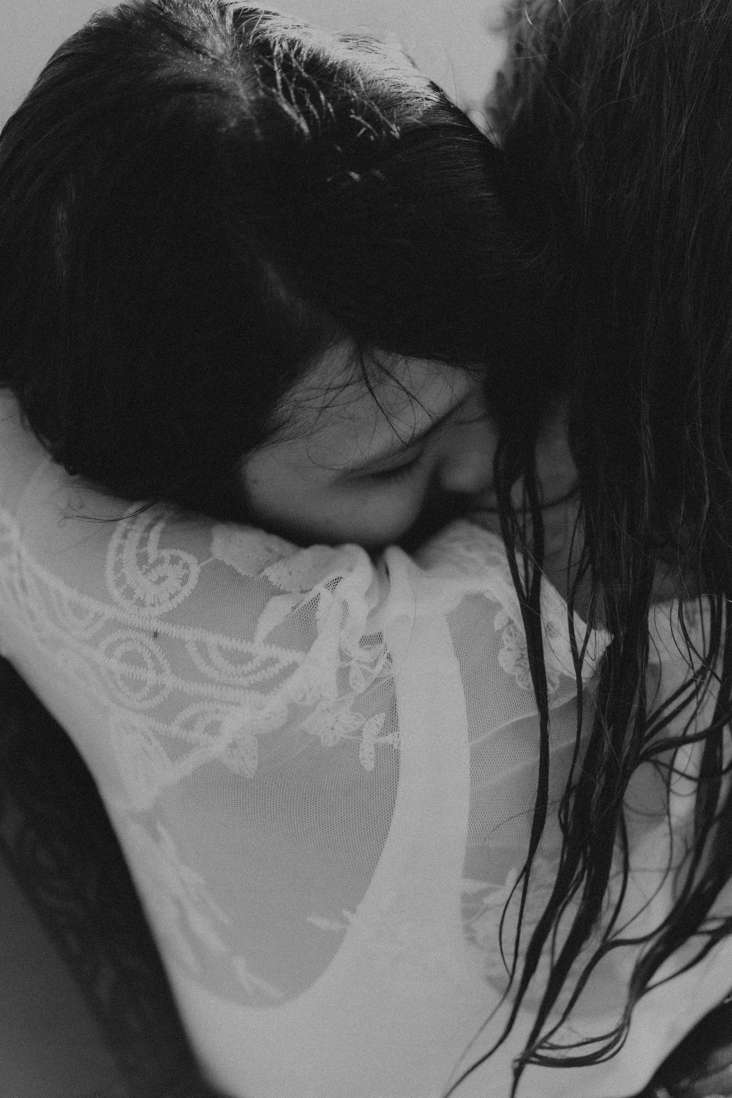 Black and white photo of two people sharing an intimate embrace, one wearing a lace top with long dark hair.