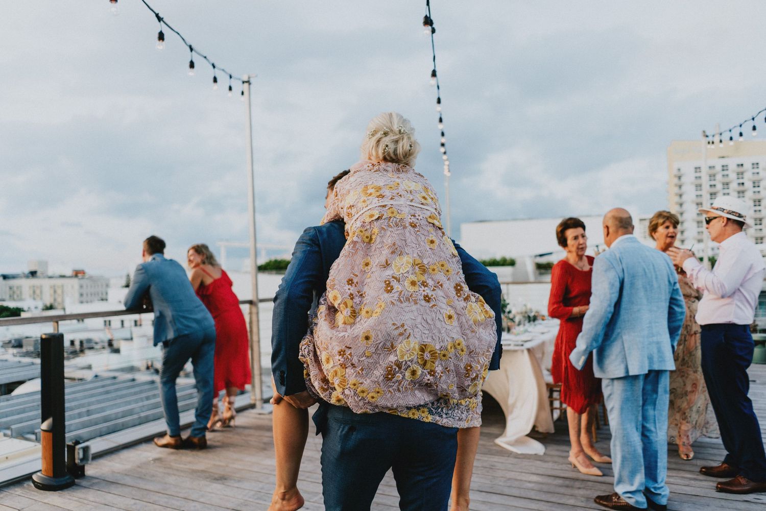 Guests socializing on a rooftop venue during an outdoor wedding reception with string lights overhead.
