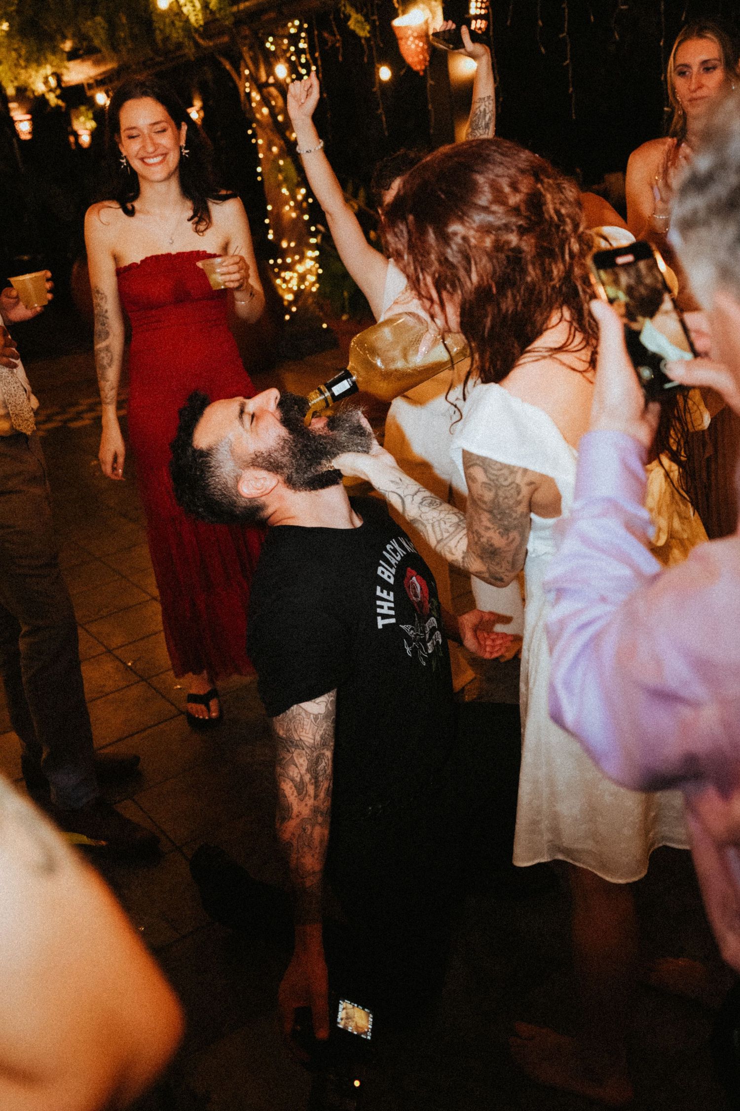 Guests dancing and celebrating at an outdoor wedding reception at night with string lights in the background.