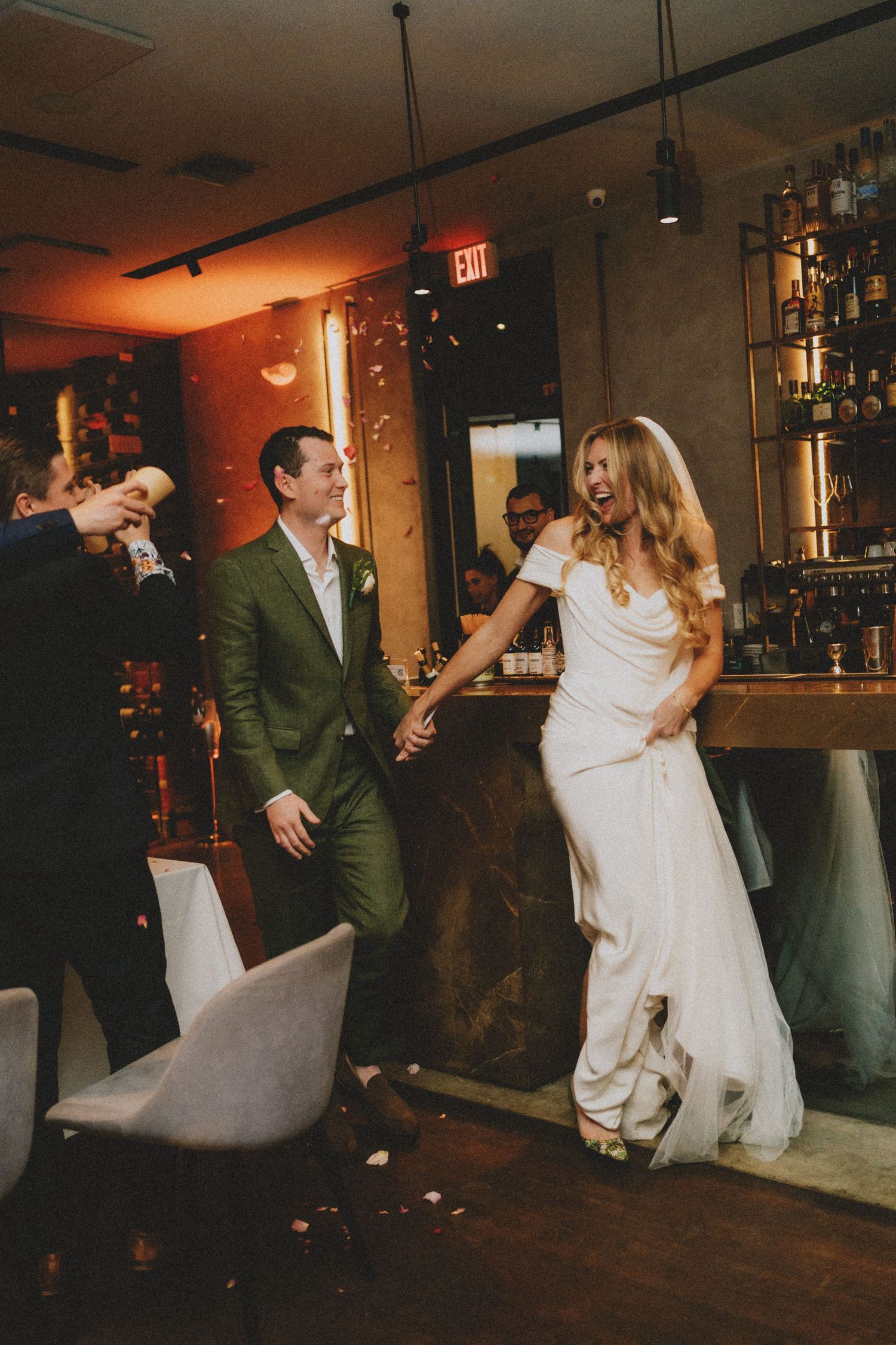 Bride and groom hold hands laughing as they enter their wedding reception at an elegant bar venue.