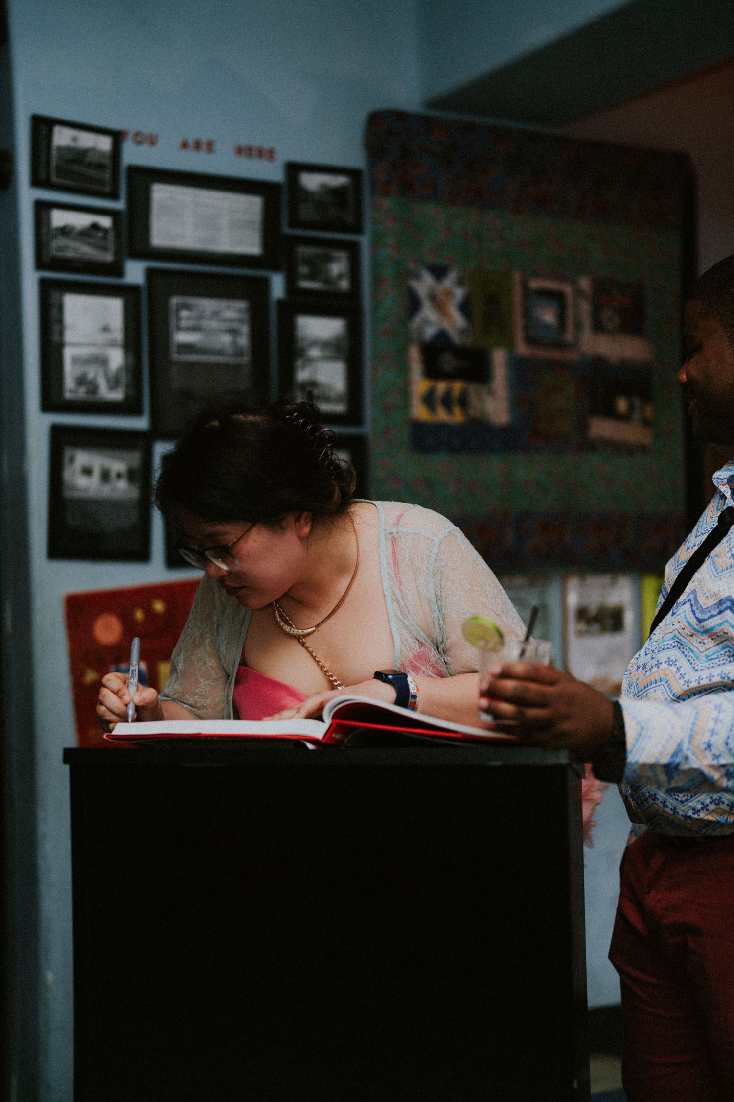 Woman writing in a red guest book at a museum exhibit with historical photos displayed on the wall.