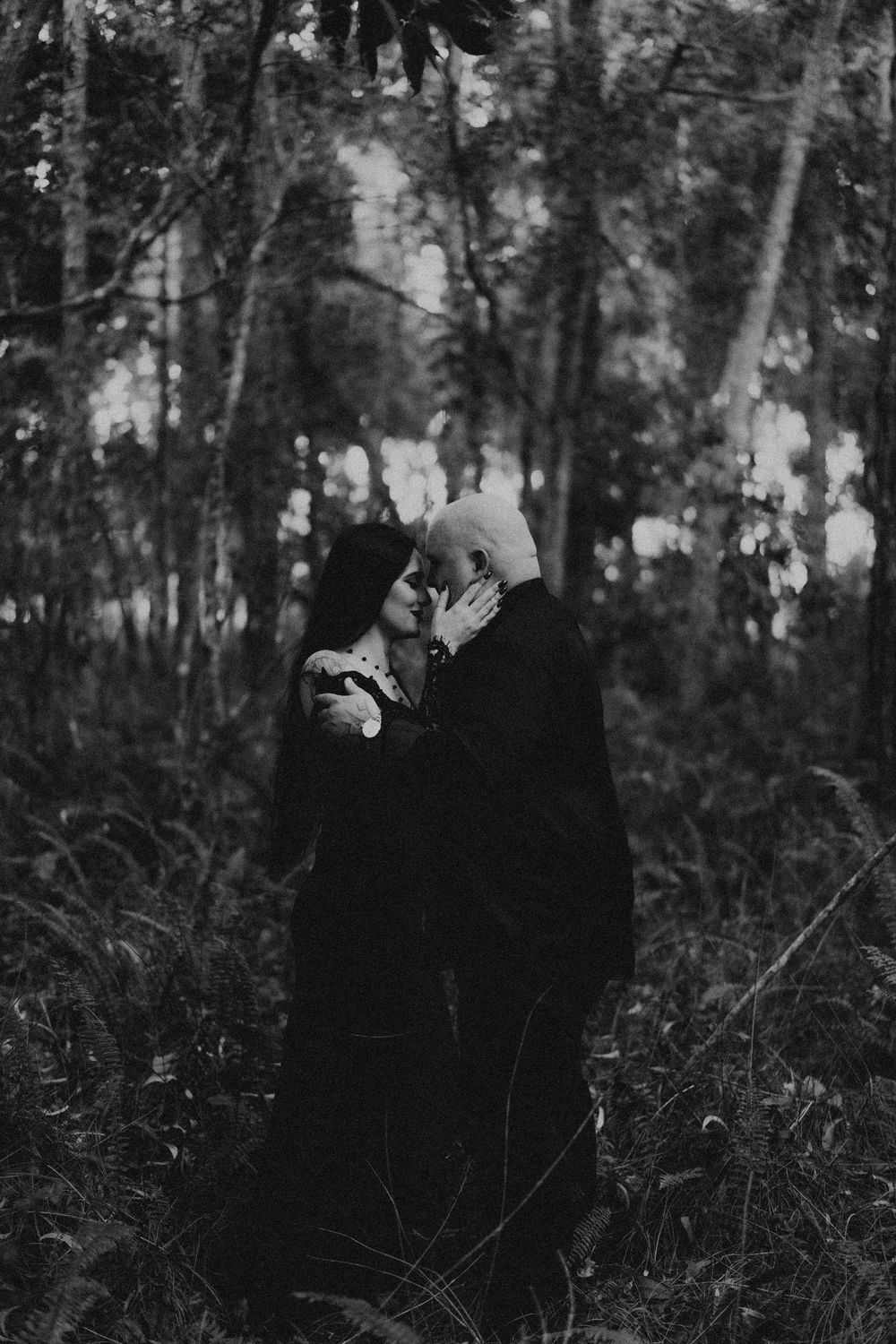 Romantic black and white photo of couple in dark forest setting.