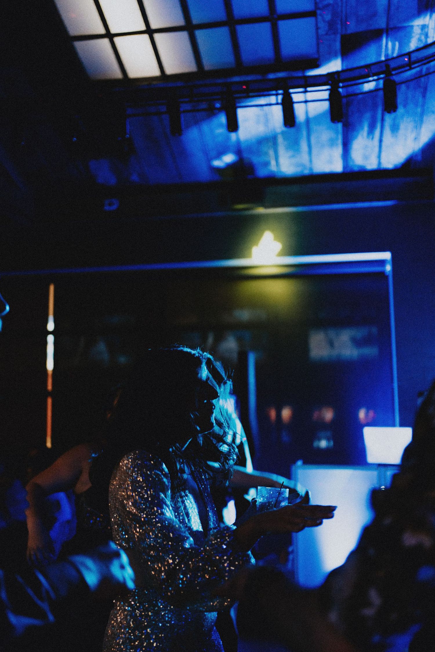 Bride in a glittering sequin gown dances under dramatic blue lighting during a lively wedding reception.