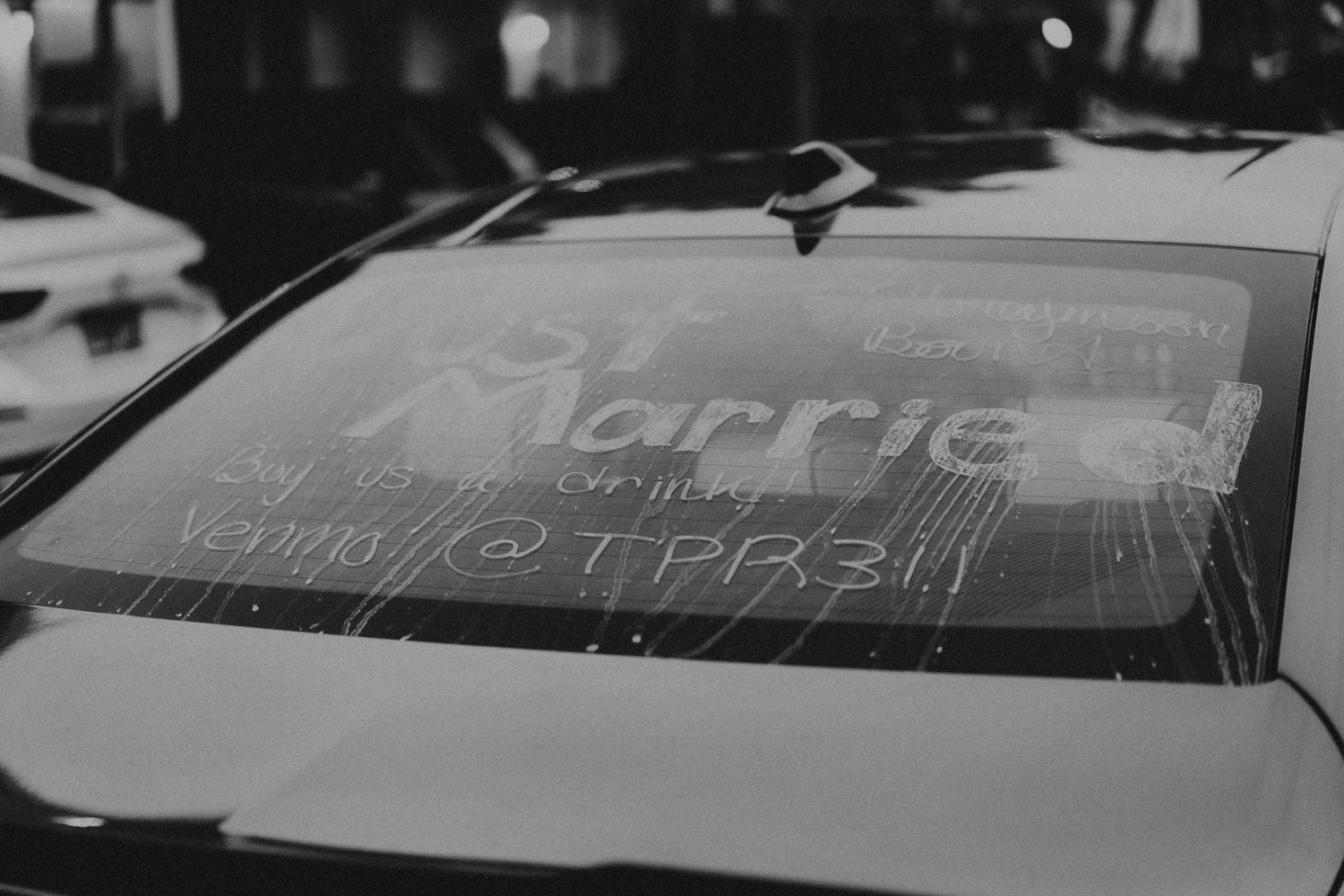 Black and white close-up of a car windshield with Just Married written in white paint.